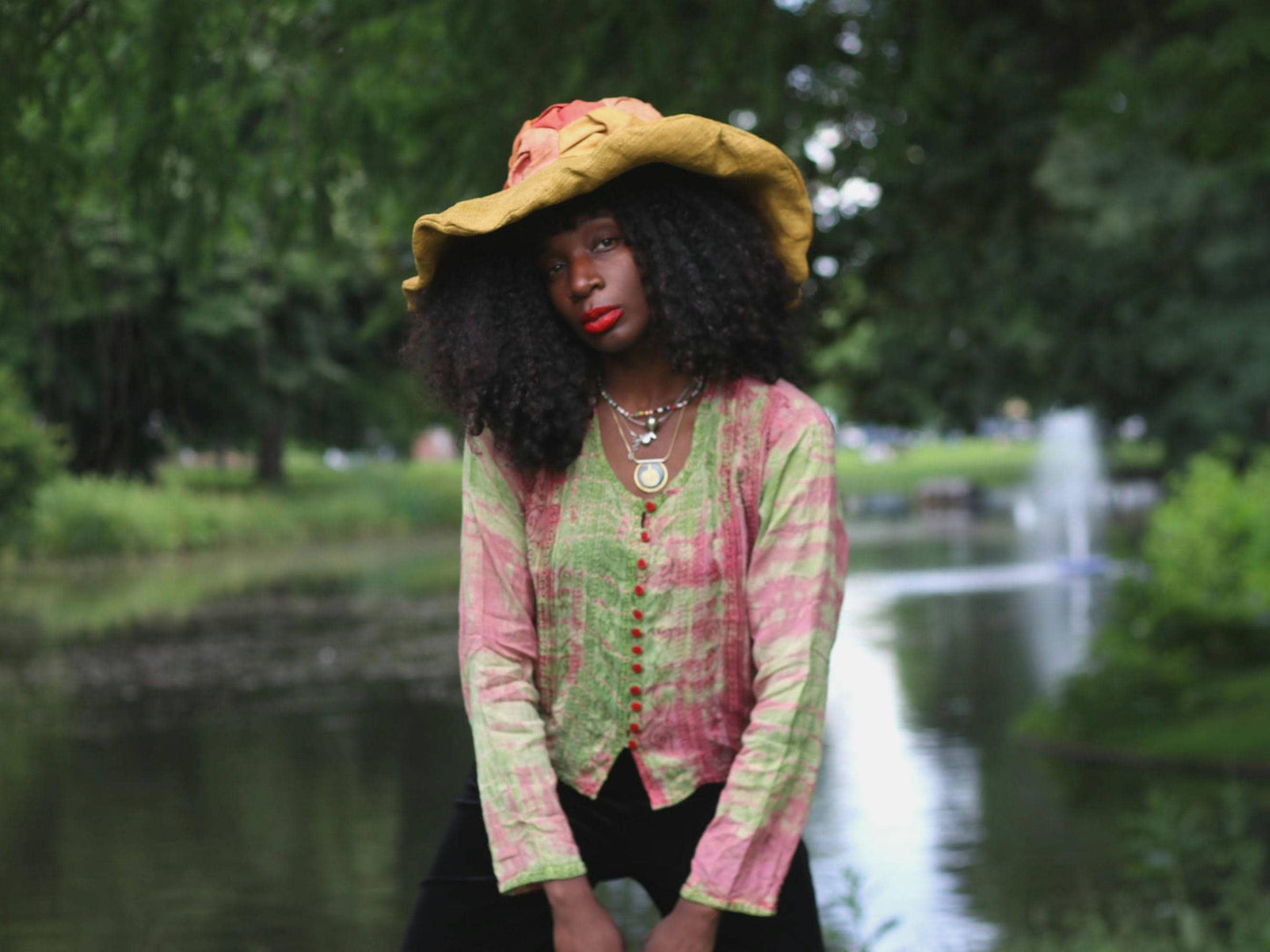 Female model in a vintage 90s pink and green tie-dye printed top and large straw hat photogrpahed by a pond.