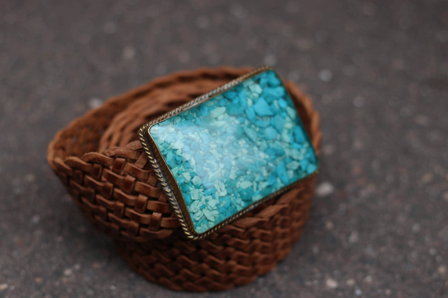 The turquoise mosaic buckle on a braided vintage brown leather belt, seen from an angle.