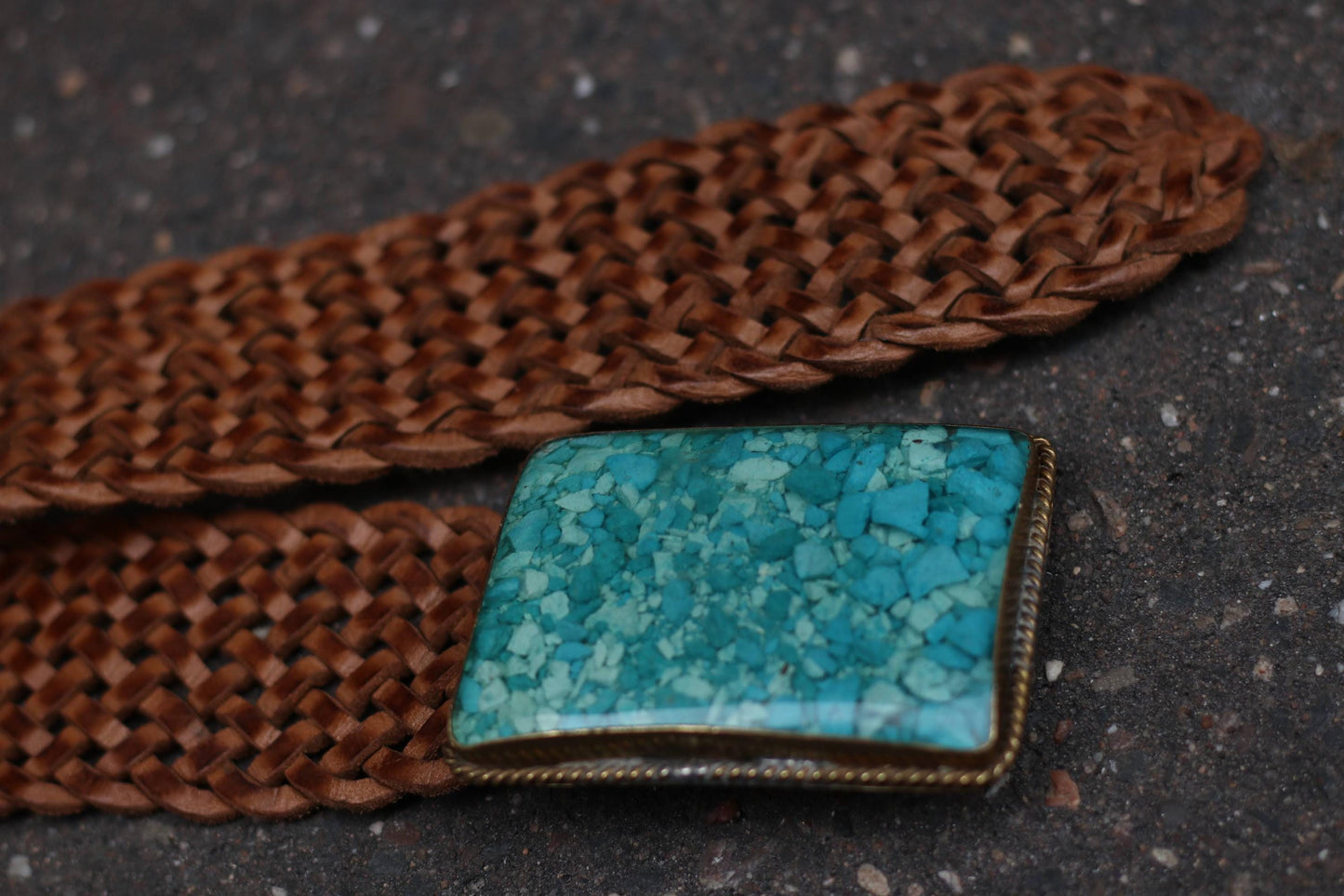 Detailed close-up of the intricate braiding and mosaic blue buckle on the brown leather belt.