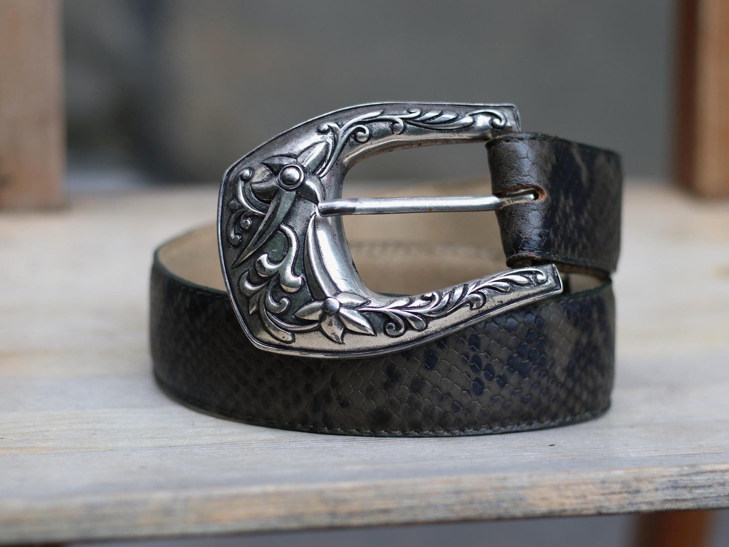 Vintage 70s brown leather belt with ornate silver western buckle photographed on a brown rustic chair against a grey wall