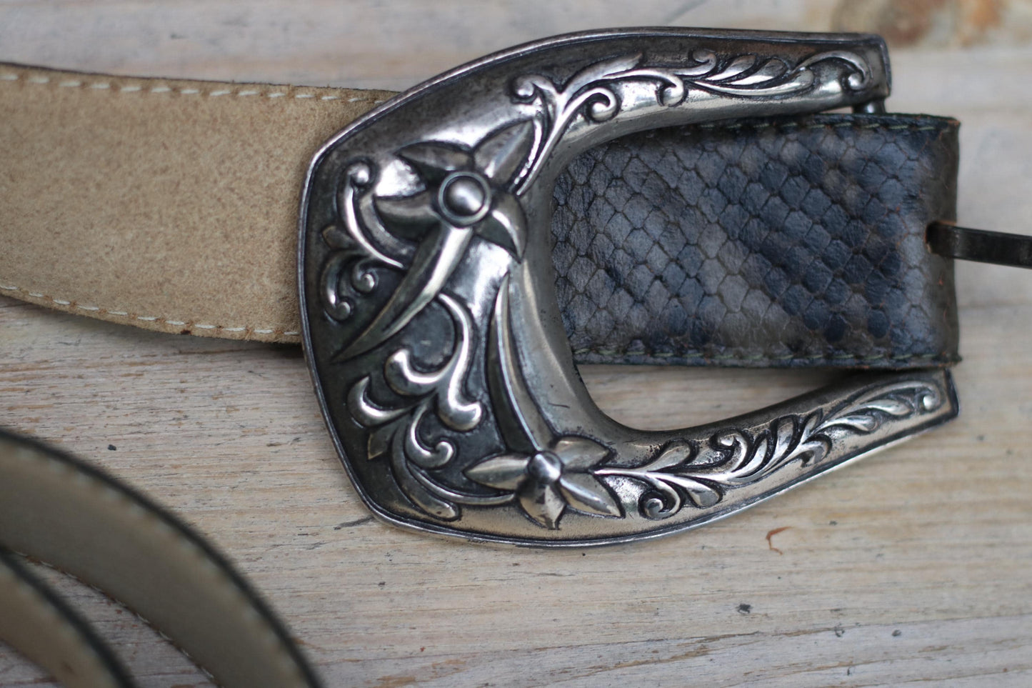 Close-up of the ornate silver western belt buckle with intricate floral and scroll details, showing its unique vintage craftsmanship.