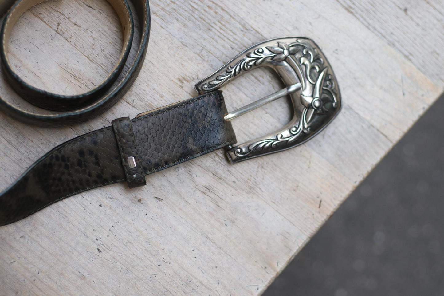 Detailed perspective of a vintage tooled leather belt with an ornate silver western buckle highlighting its decorative elements and texture.