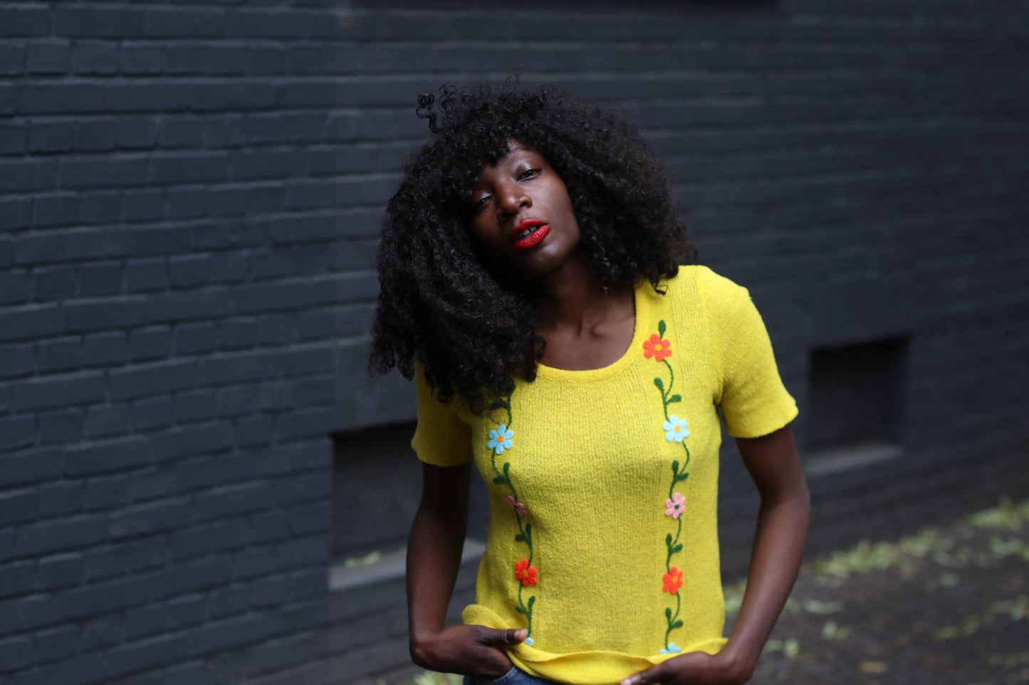 Retro vintage yellow short sleeved top with vertical flower embroidery on a female model photographed outdoors against a grey wall