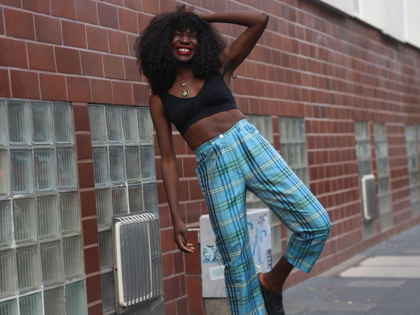 A female model posing in vintage Peter Hahn silk pants featuring a vibrant blue and green plaid pattern, paired with a black crop top.