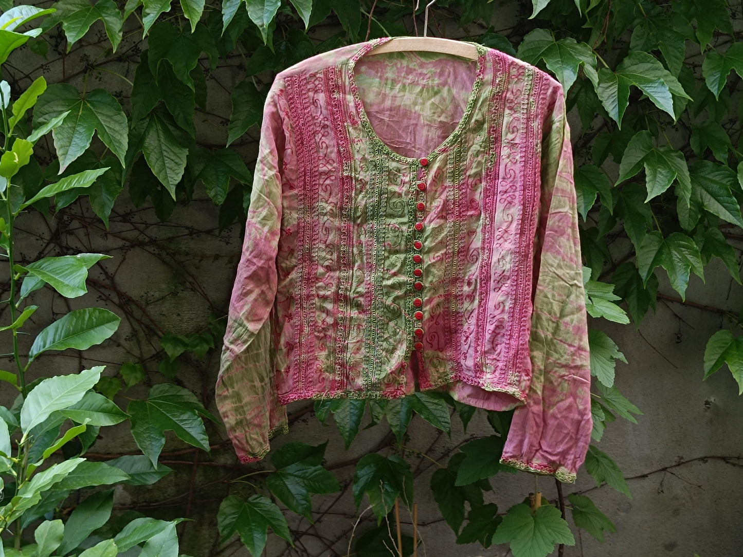 Retro tie-dye boho blouse with pink and green patterned photographed hanging outdoors on a clothing line with leaves in the background. The still life image showcases the print and texture of the retro long-sleeved top.