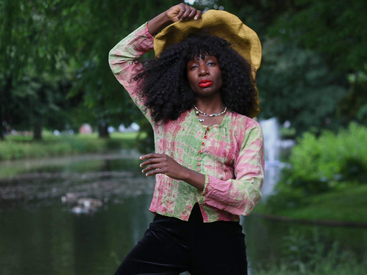 Female model in a vintage 90s pink and green printed tie-dye long sleeved top and large straw hat, posing outdoors near water