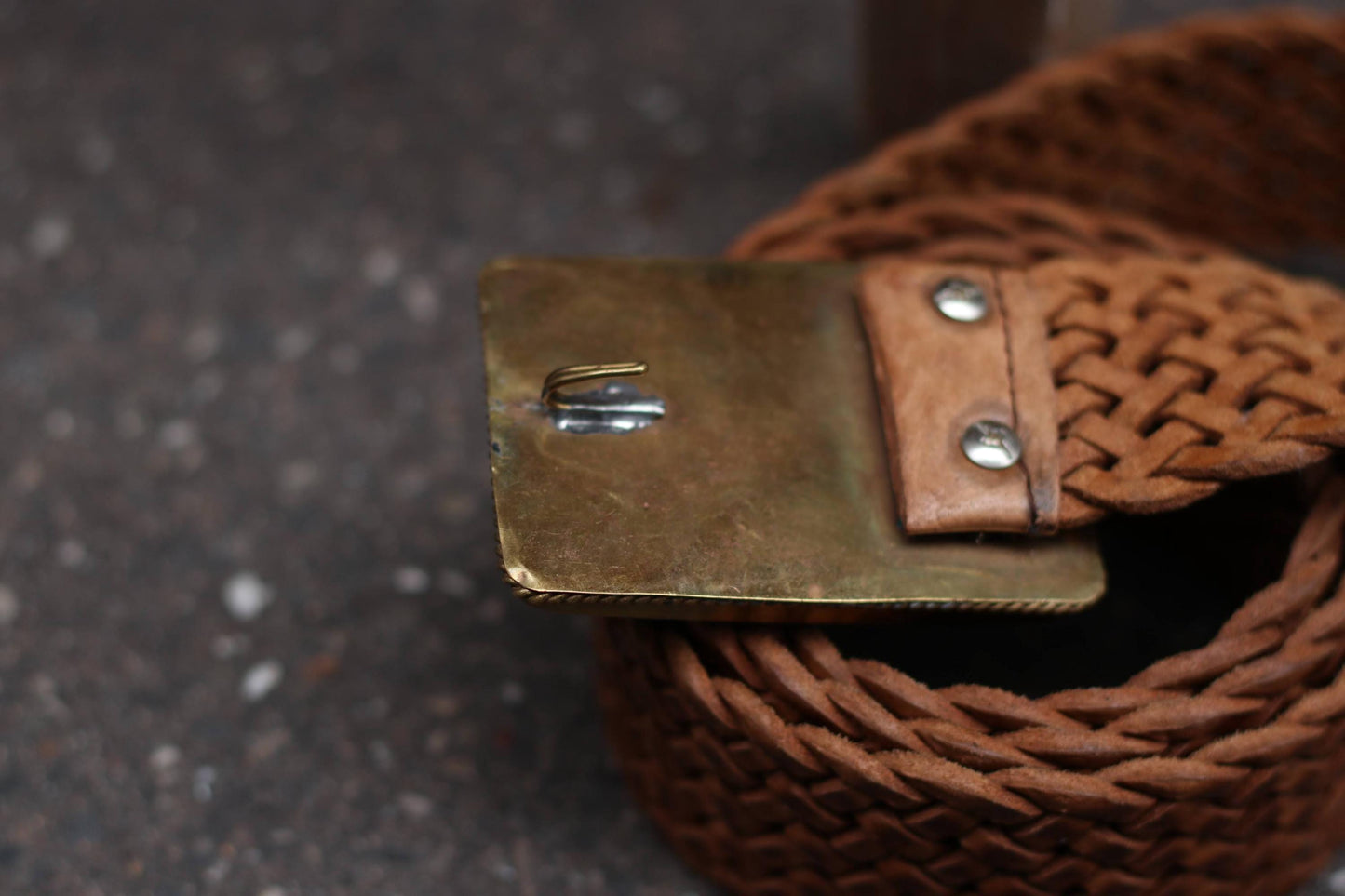 Back view of the belt buckle, showing the brass-toned hardware and leather attachment.