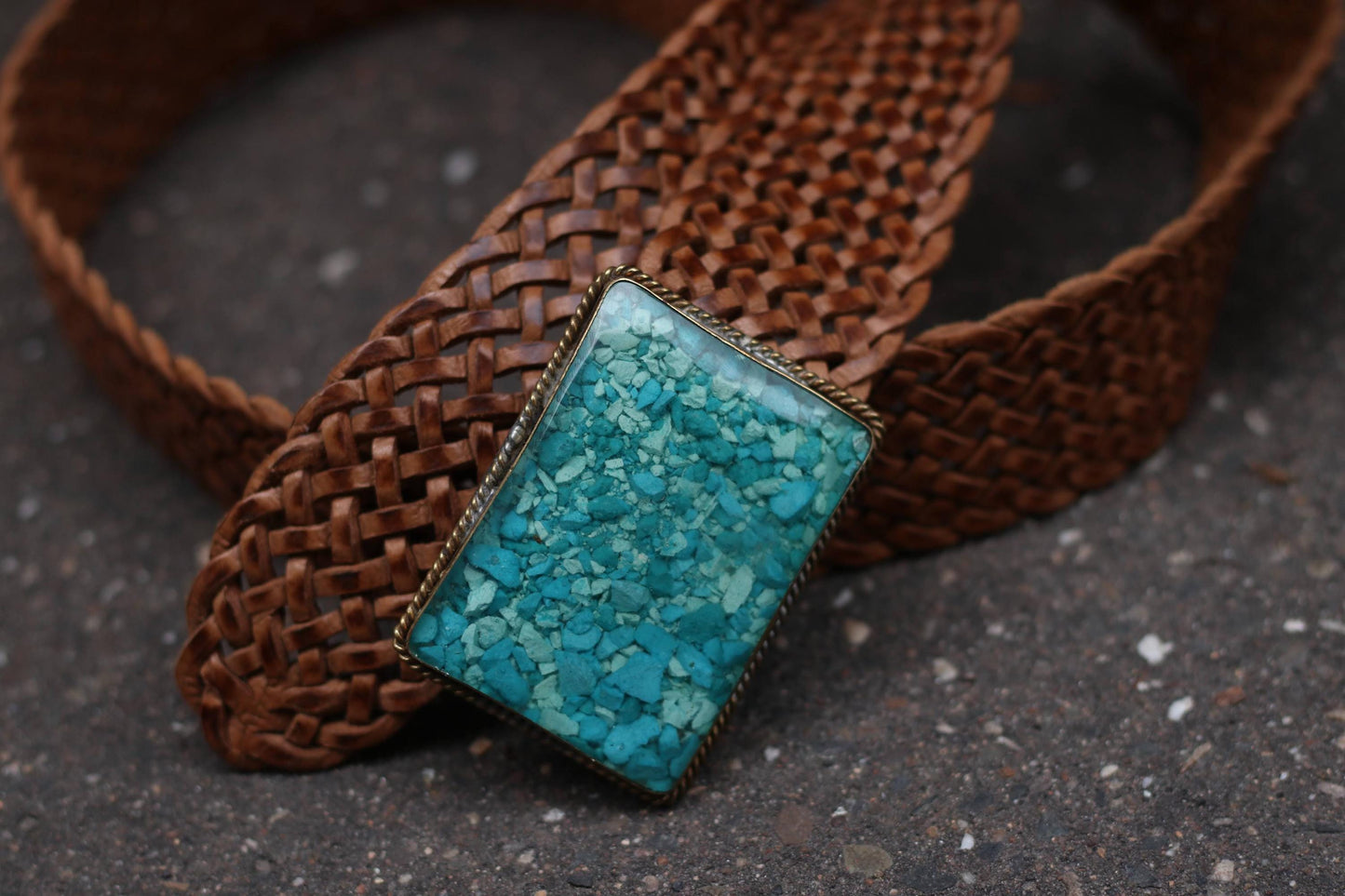 Braided brown vintage retro leather belt with the turquoise buckle, laid out on a dark surface.