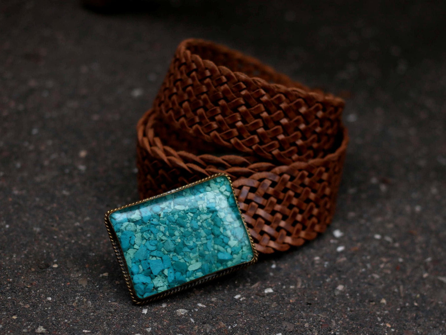 Vintage handmade braided leather belt with large turquoise mosaic buckle, coiled on a dark surface.