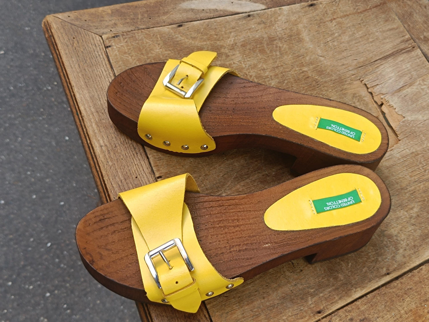 Pair of bright yellow y2k Benetton wooden clogs on a rustic wooden table.