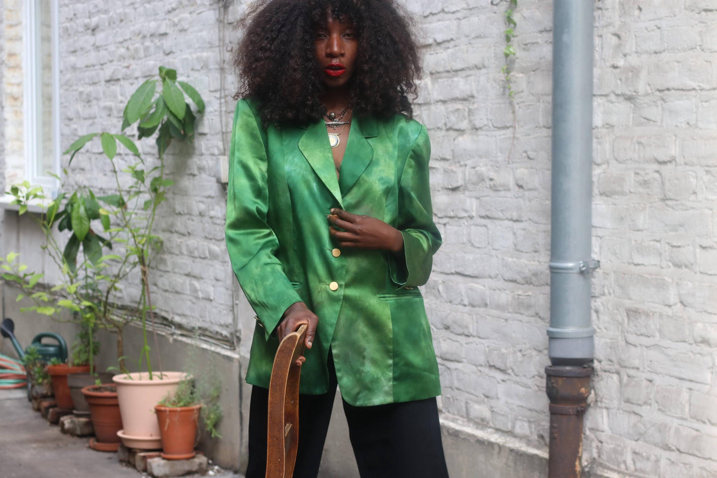 Model wearing vintage 90s emerald green silk blazer made in Germany outdoors against a white brick wall background