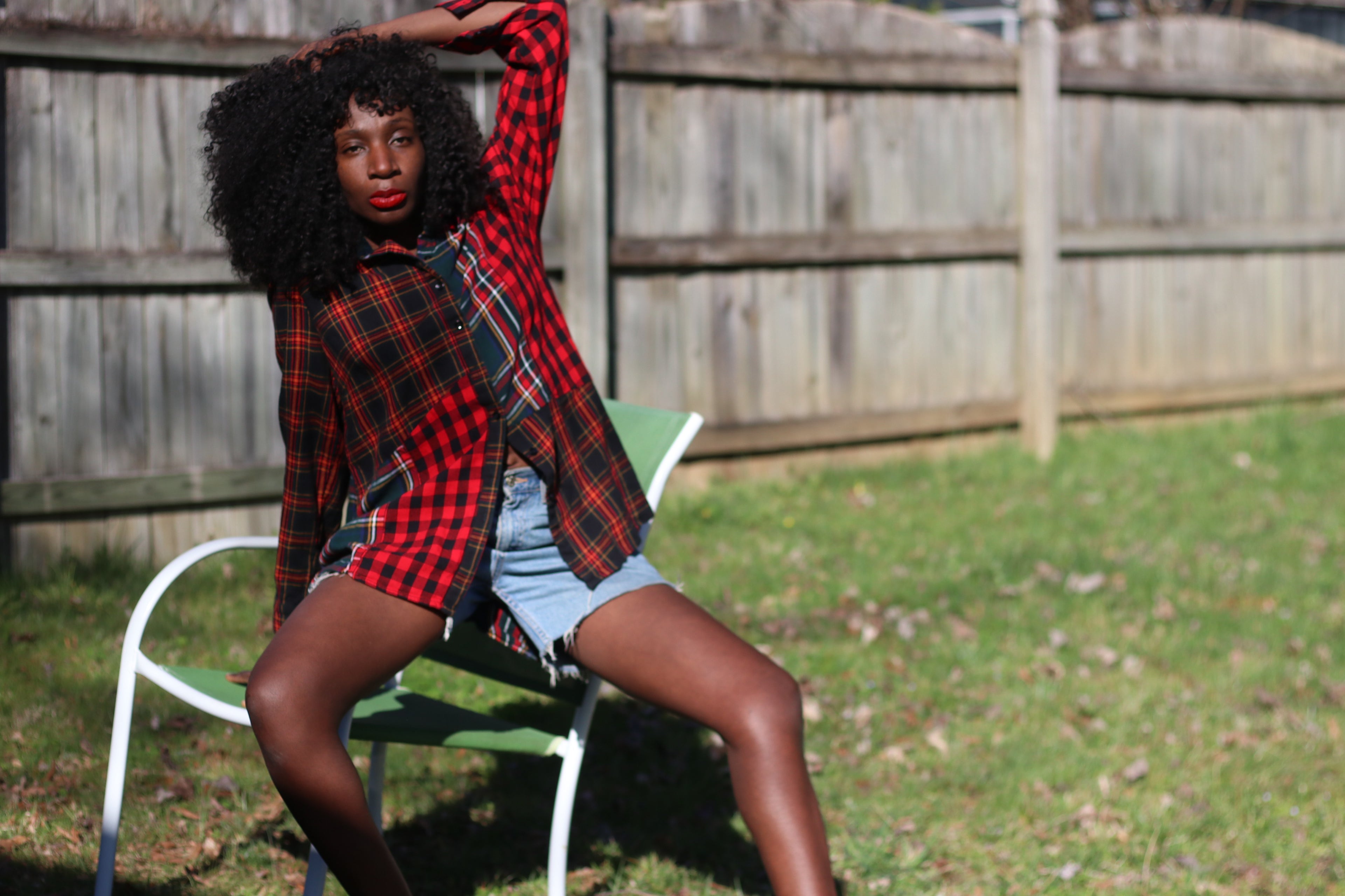 A woman with voluminous curls poses outdoors wearing a vintage Coldwater Creek plaid shirt in red and green. The relaxed-fit button-up, made from a soft viscose-cotton blend, drapes effortlessly over her denim cutoffs, creating a laid-back, edgy look