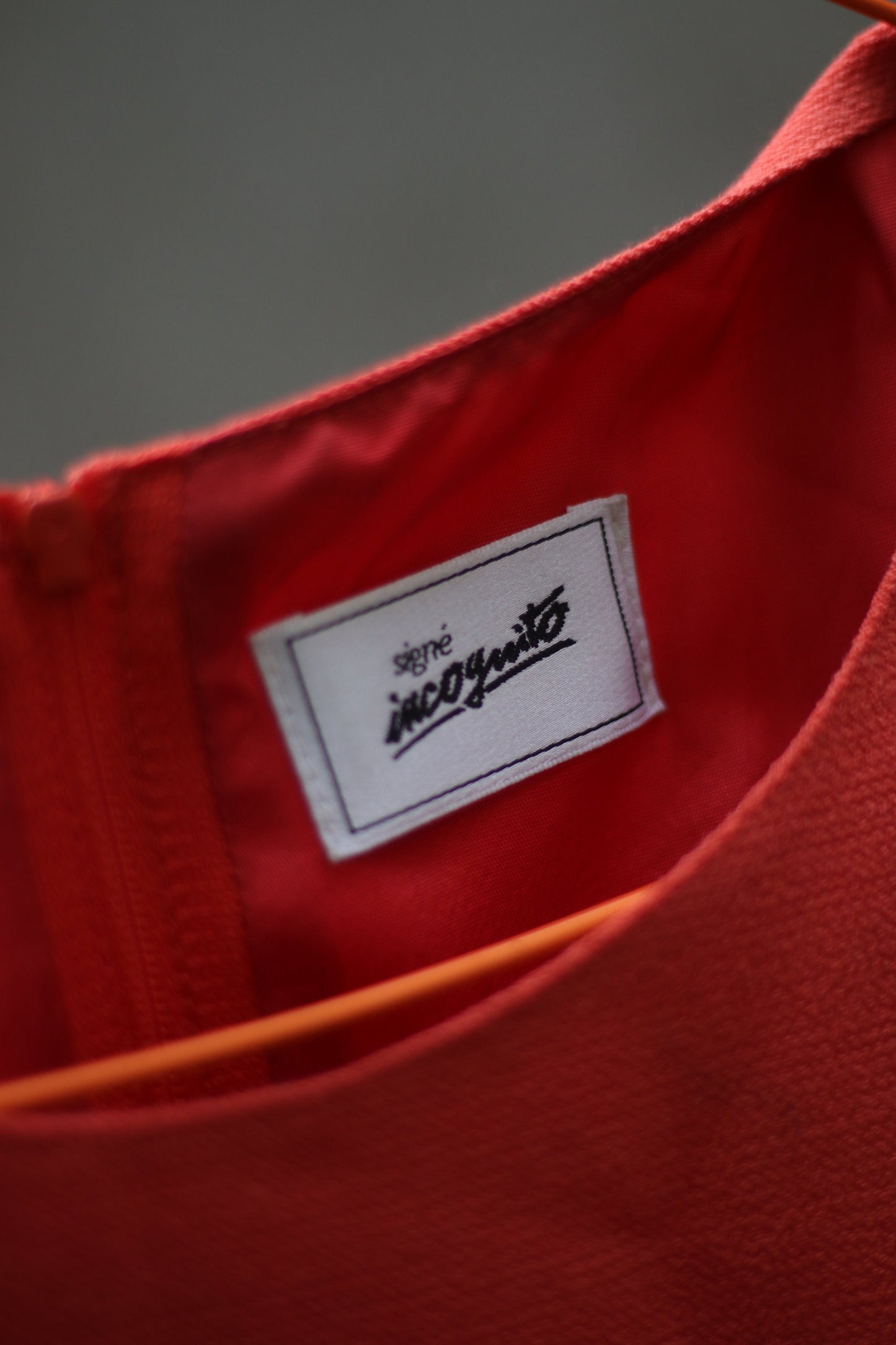 A close up of the orange sleeveless vintage dress by the brand Signe incognito is photographed outdoors on a red hanger