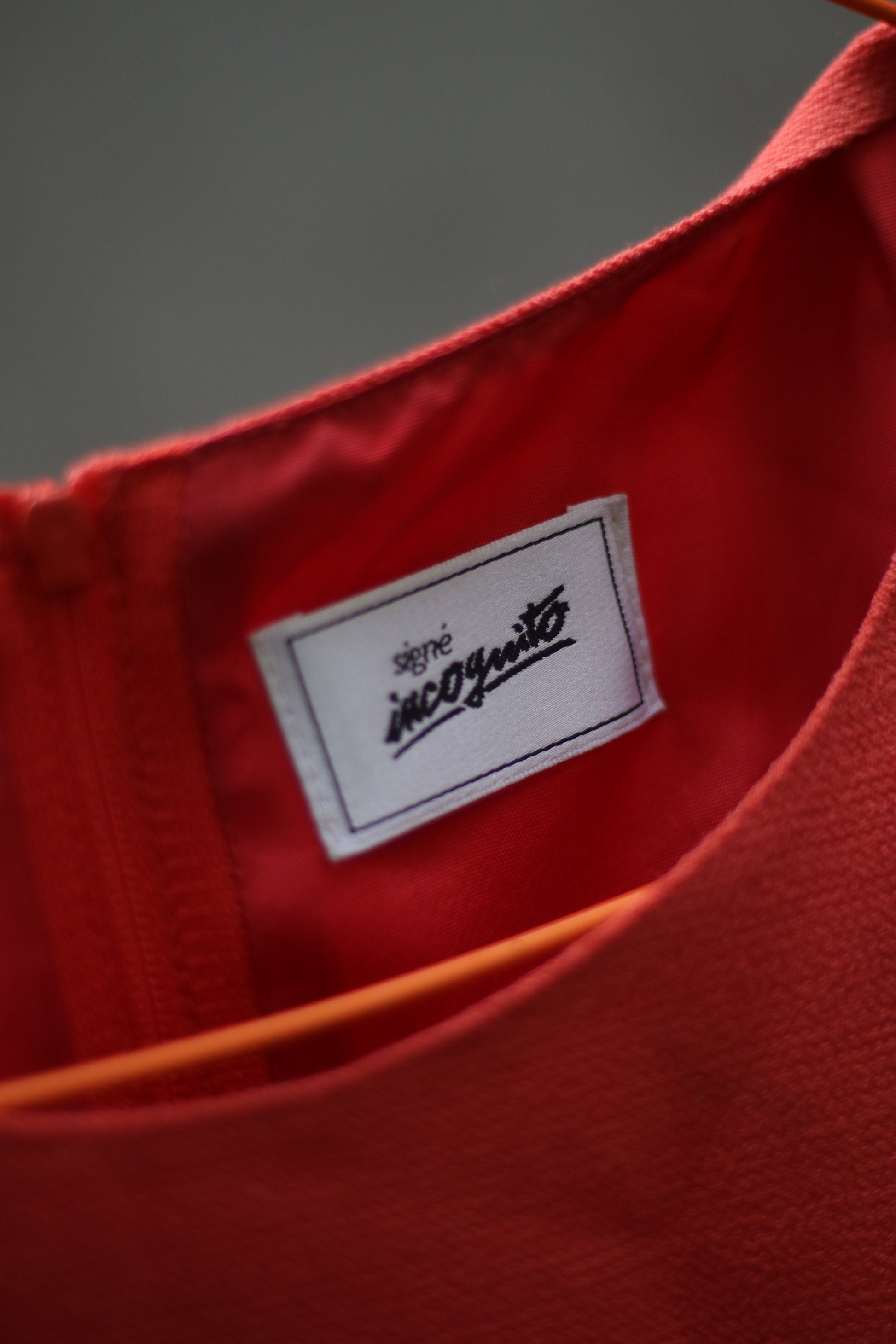 A close up of the orange sleeveless vintage dress by the brand Signe incognito is photographed outdoors on a red hanger