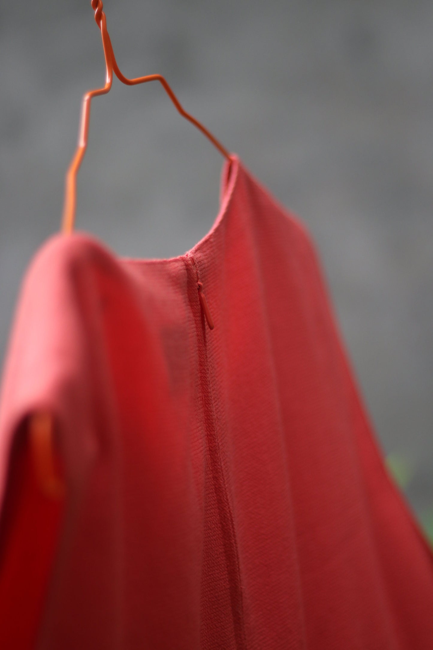 Close up of the backof and orange sleeveless vintage dress by the brand Signe incognito is photographed outdoors on a red hanger