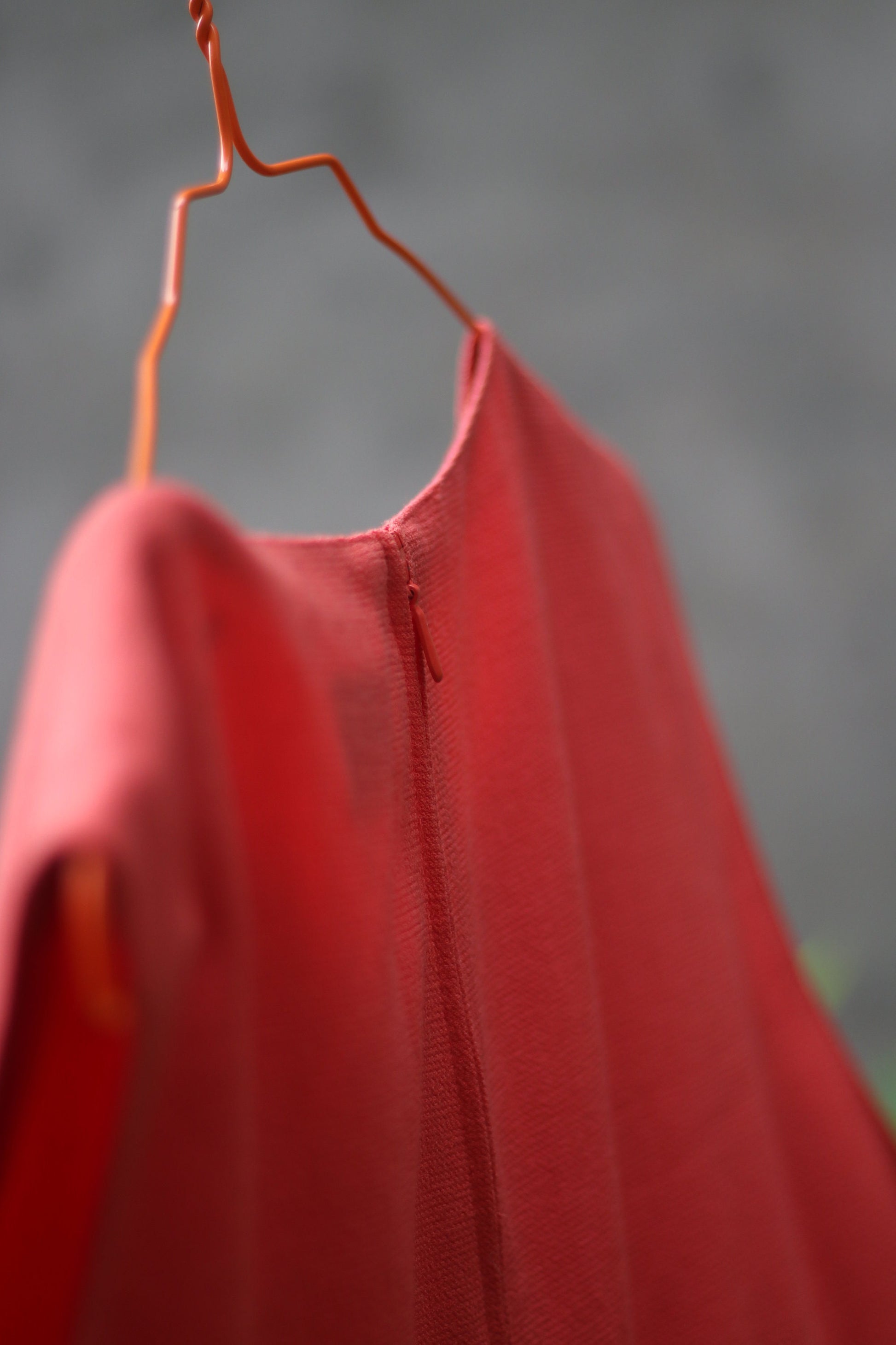 Close up of the backof and orange sleeveless vintage dress by the brand Signe incognito is photographed outdoors on a red hanger