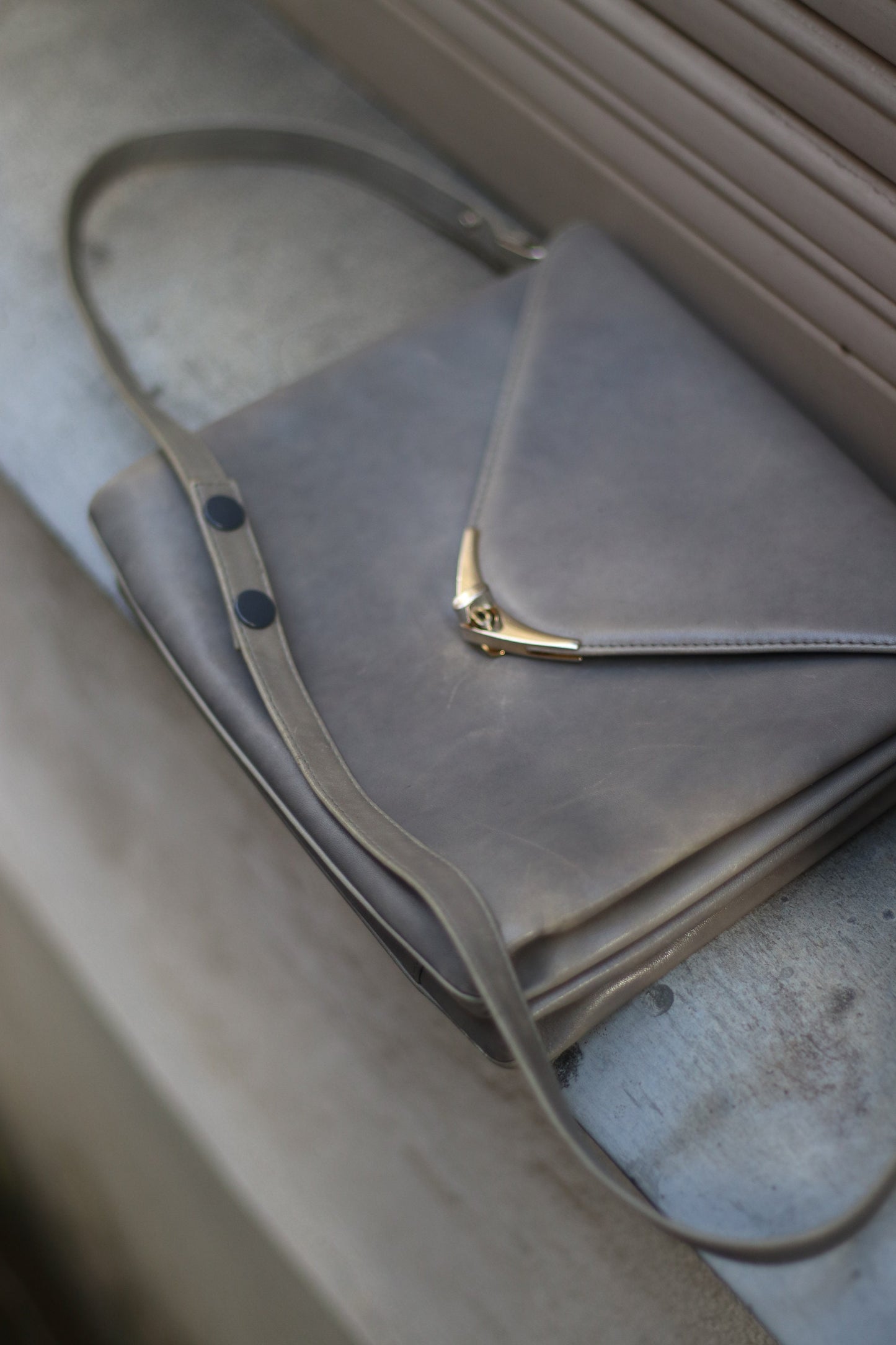 A grey compact bag from the 70s photographed lying flat a grey slate stone. The minimalist leather bag for women is by the german brand Nierhaus. Small in size, the bag has adjustable straps.