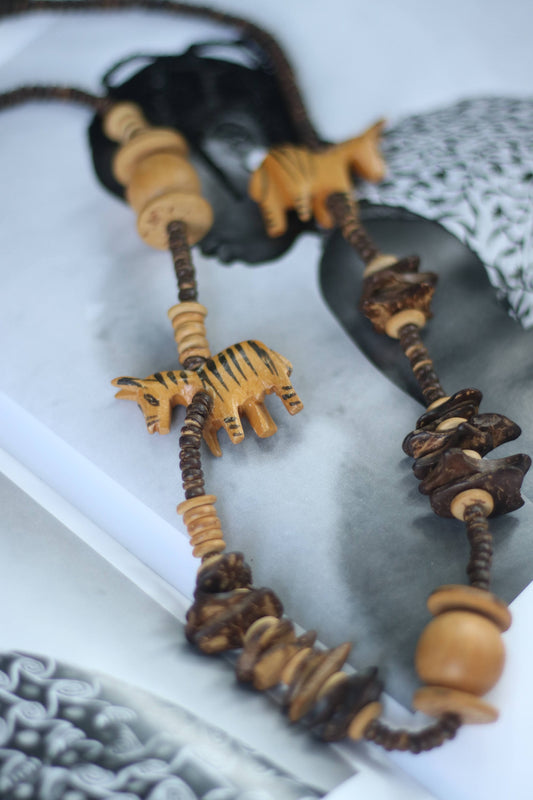 vintage handmade necklace featuring hand-carved wooden animal charms with tribal-style stripes, strung on an earthy-toned beaded cord. Rich in bohemian and artisan charm, it’s a unique statement accessory inspired by global craftsmanship.