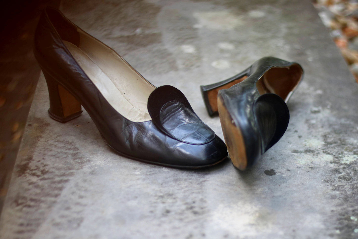 Vintage black leather high-heeled shoes with a rounded toe and mid heel, showcased on a concrete surface. Perfect for retro fashion enthusiasts and classic footwear collectors.
