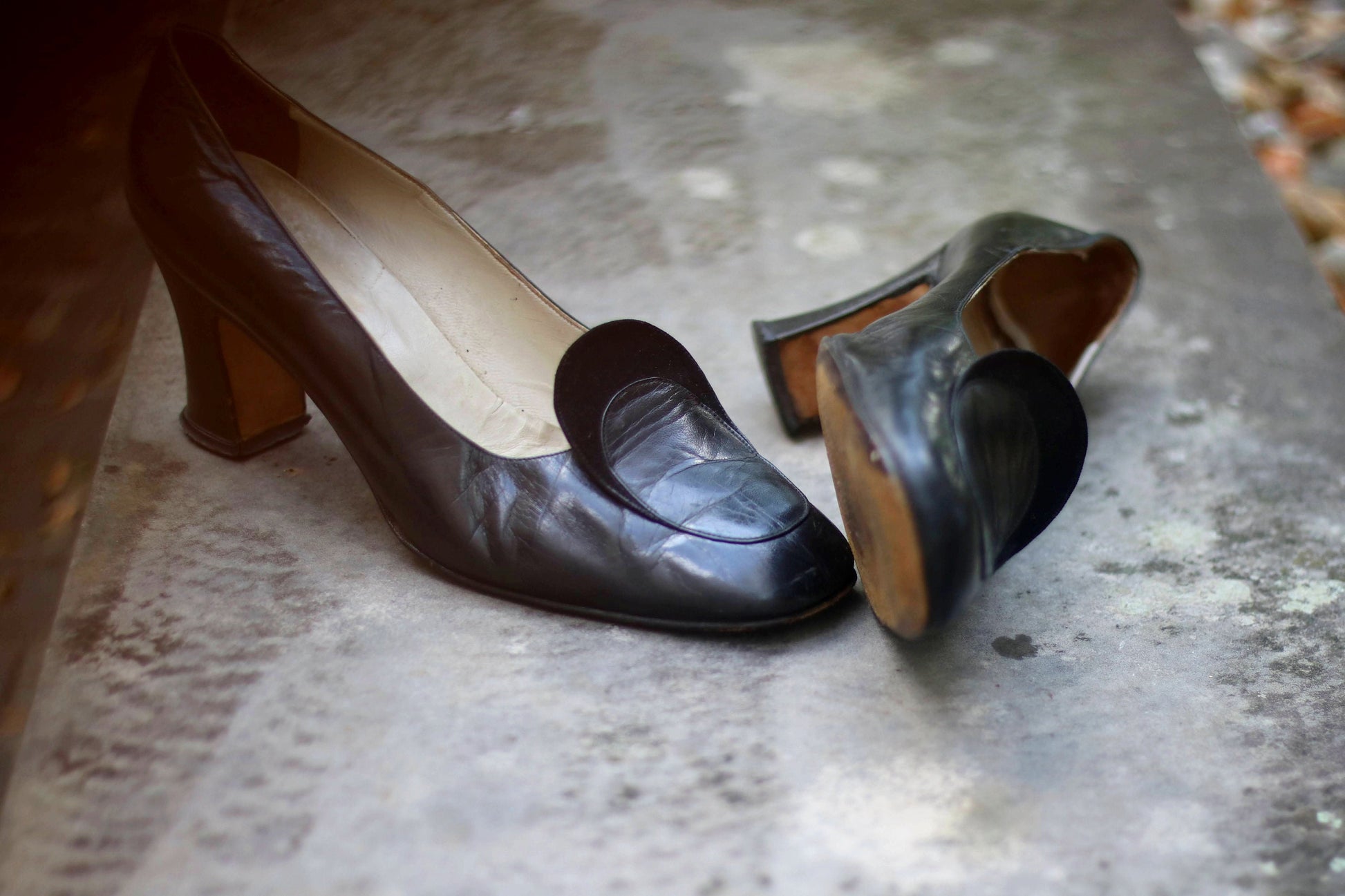 Vintage black leather high-heeled shoes with a rounded toe and mid heel, showcased on a concrete surface. Perfect for retro fashion enthusiasts and classic footwear collectors.