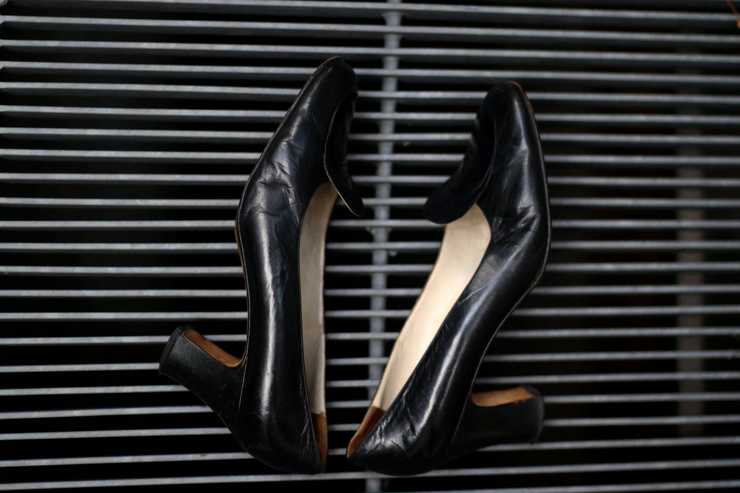 Vintage black leather high-heeled shoes with a rounded toe and mid heel, showcased on a concrete surface. Perfect for retro fashion enthusiasts and classic footwear collectors.