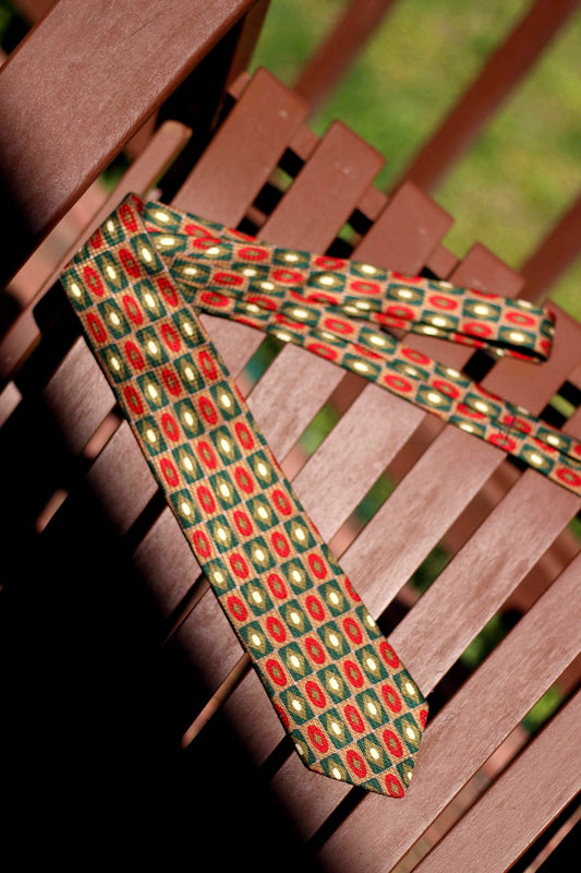 A vintage red and brown Landsend tie photographed on top of a wooden bench. The tie is silk and as polka dotted print.