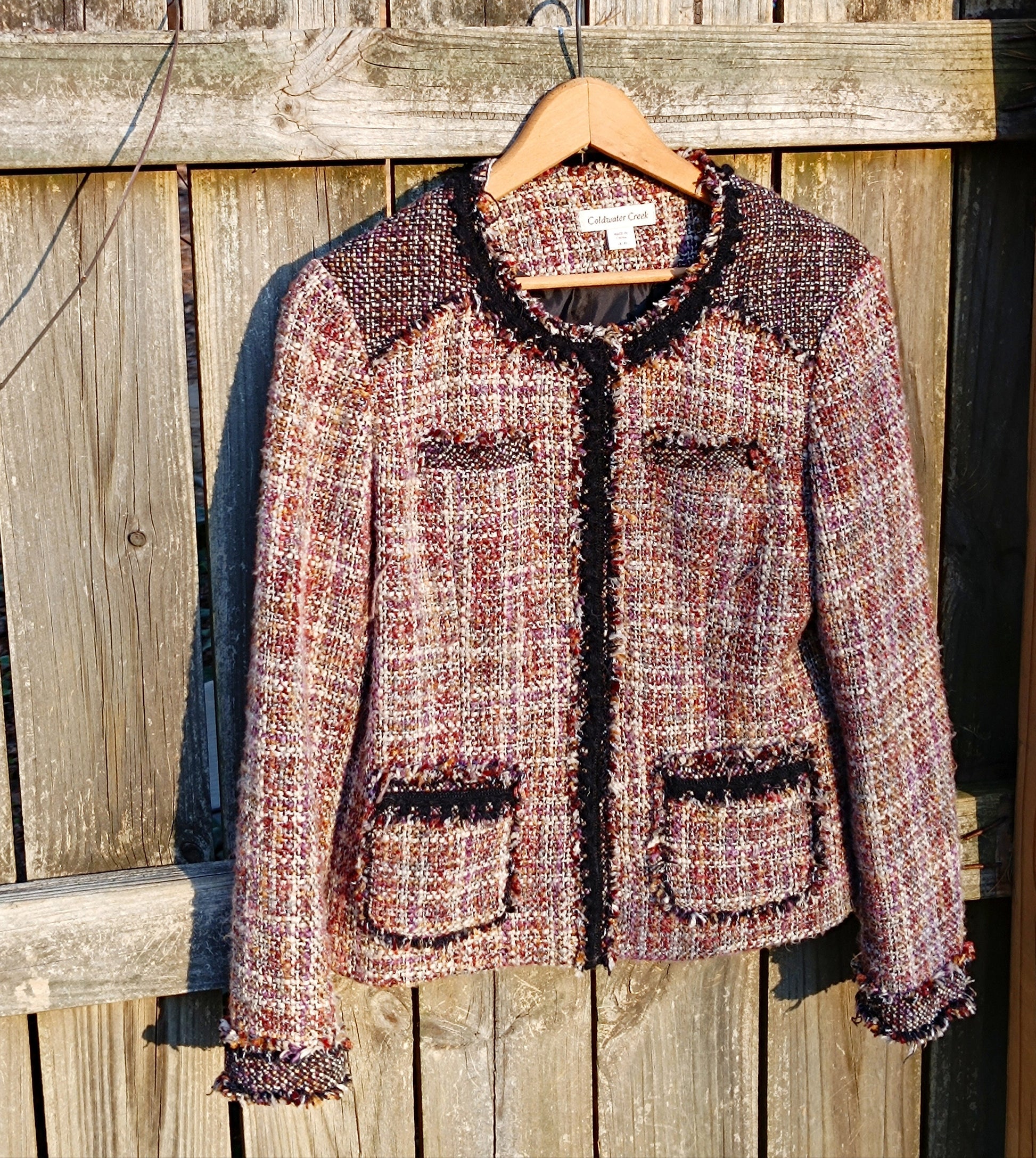 Textured vintage 90s  tweed blazer by Coldwater Creek in shades of pink, cream, and black hanging against a rustic wooden fence.