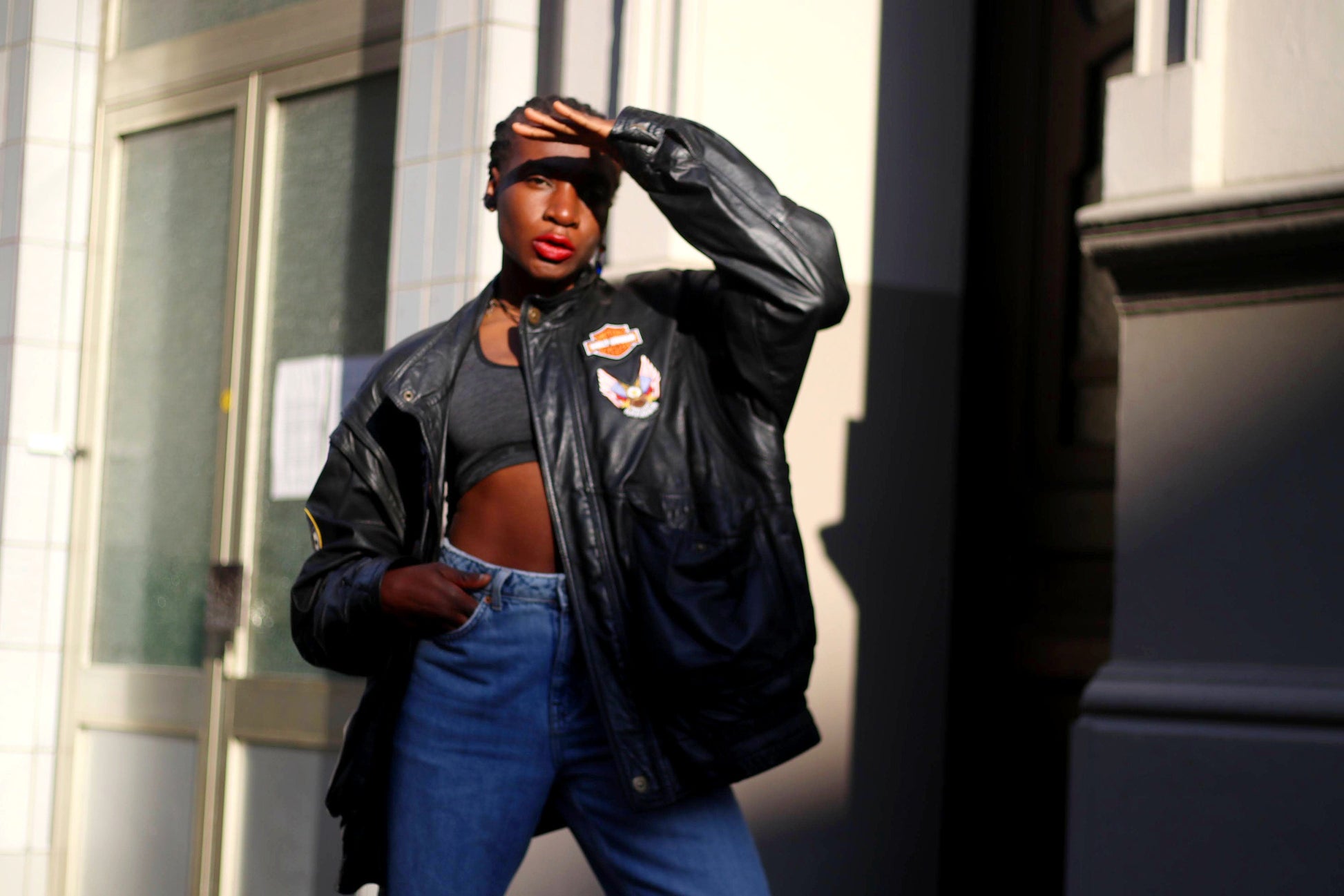 Person of African Heritage wearing a black vintage biker leather jacket with an embroidered details, standing in front of a wall . Street style fashion with casual urban backdrop