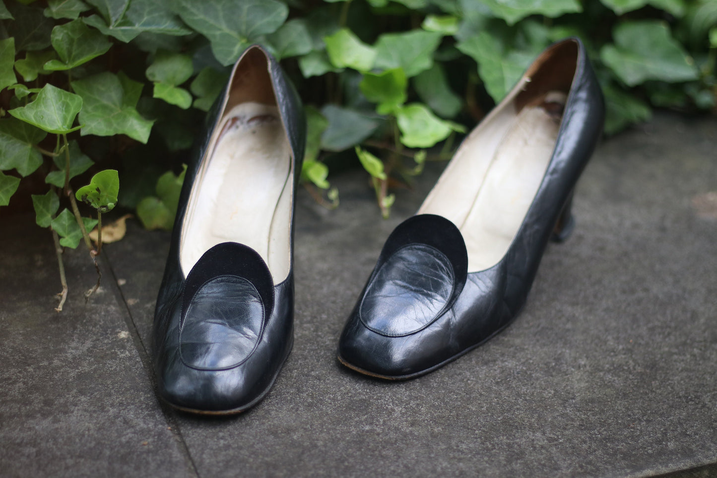 Vintage black leather high-heeled shoes with a rounded toe and mid heel, showcased on a concrete surface. Perfect for retro fashion enthusiasts and classic footwear collectors.
