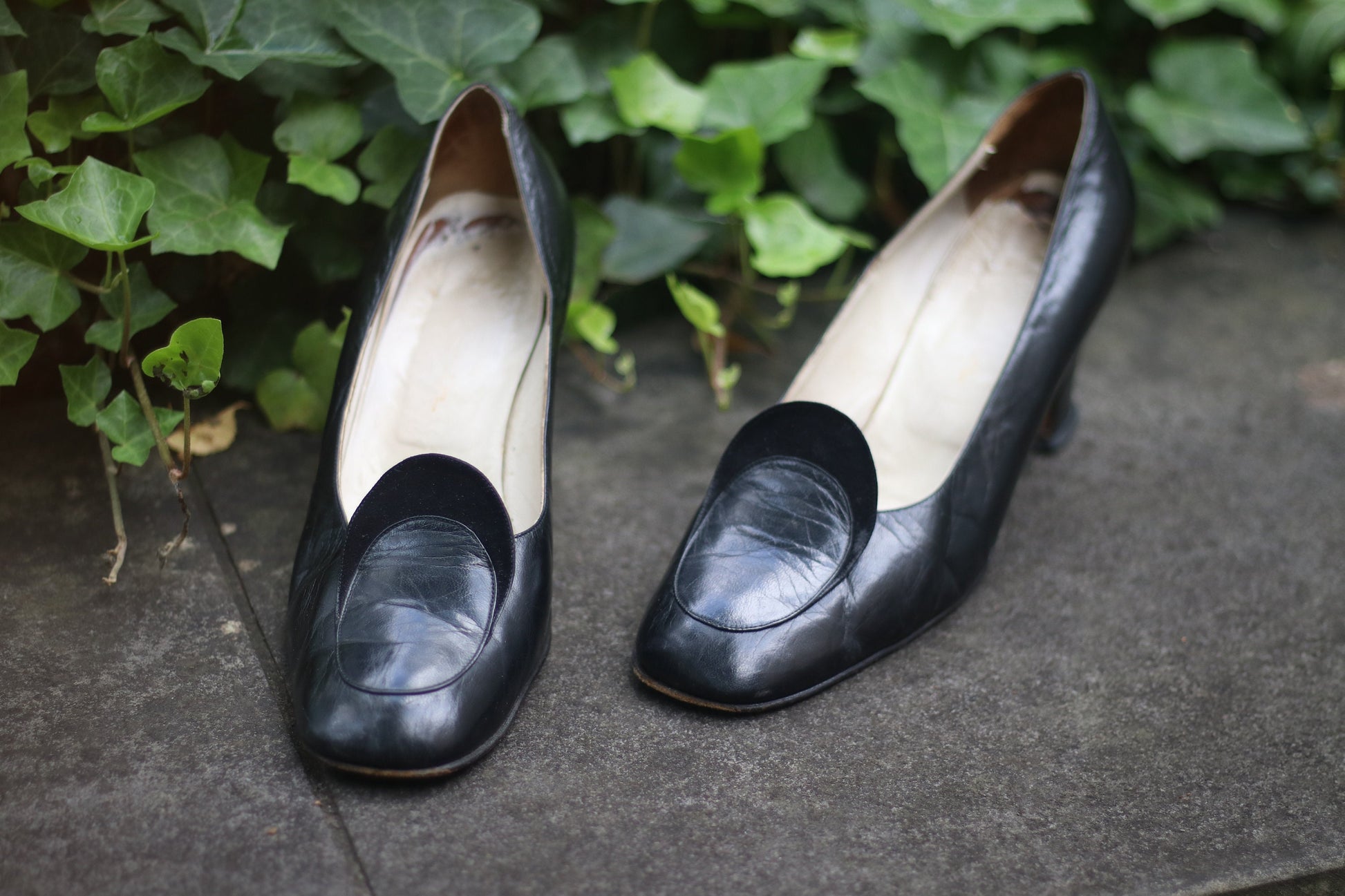 Vintage black leather high-heeled shoes with a rounded toe and mid heel, showcased on a concrete surface. Perfect for retro fashion enthusiasts and classic footwear collectors.