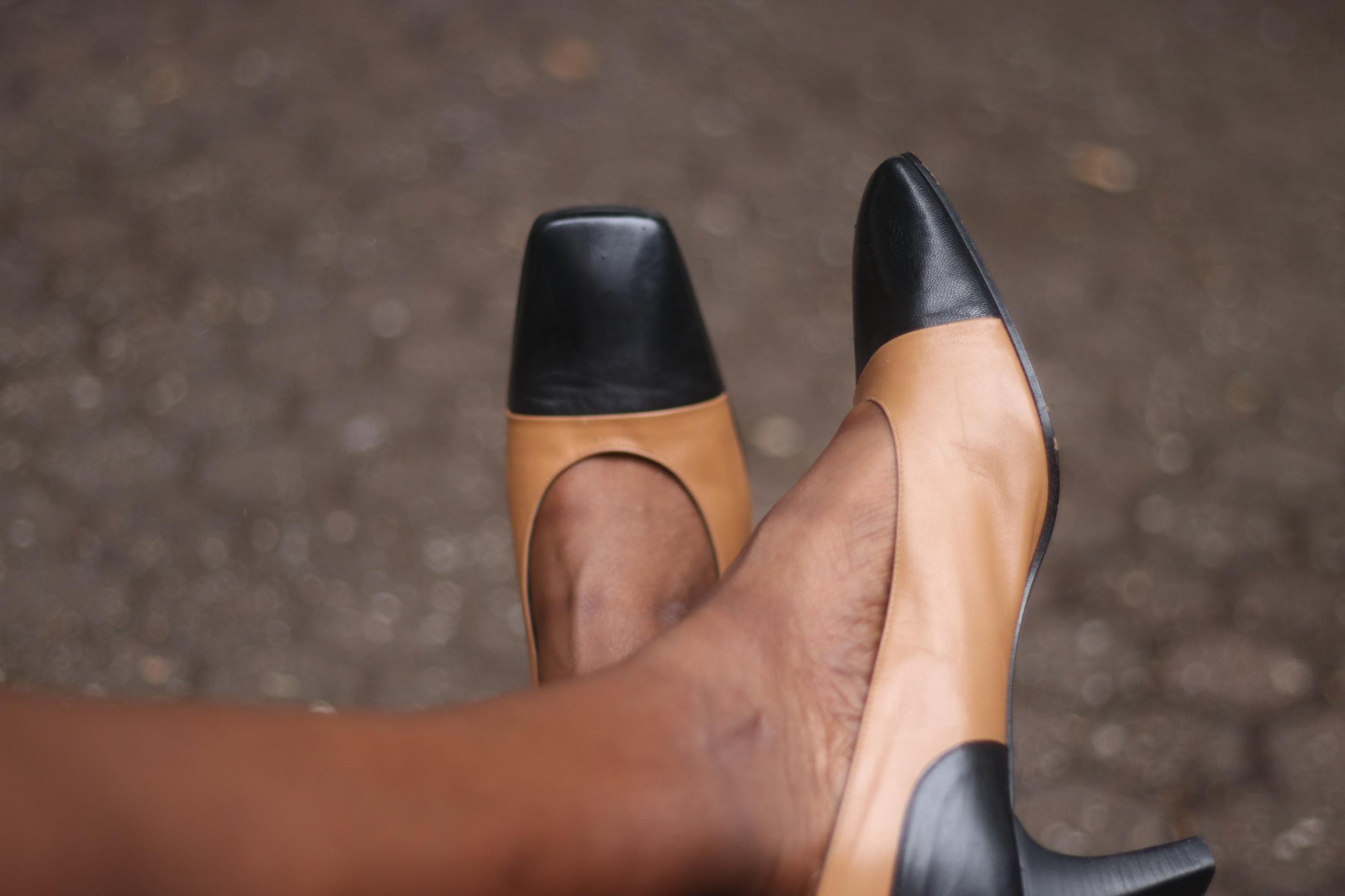 A pair of vintage two-tone high heels in brown and black on a model&#39;s feet. The brand is Tanja Jannetti. The chic pumps are photographed against a blurred background.