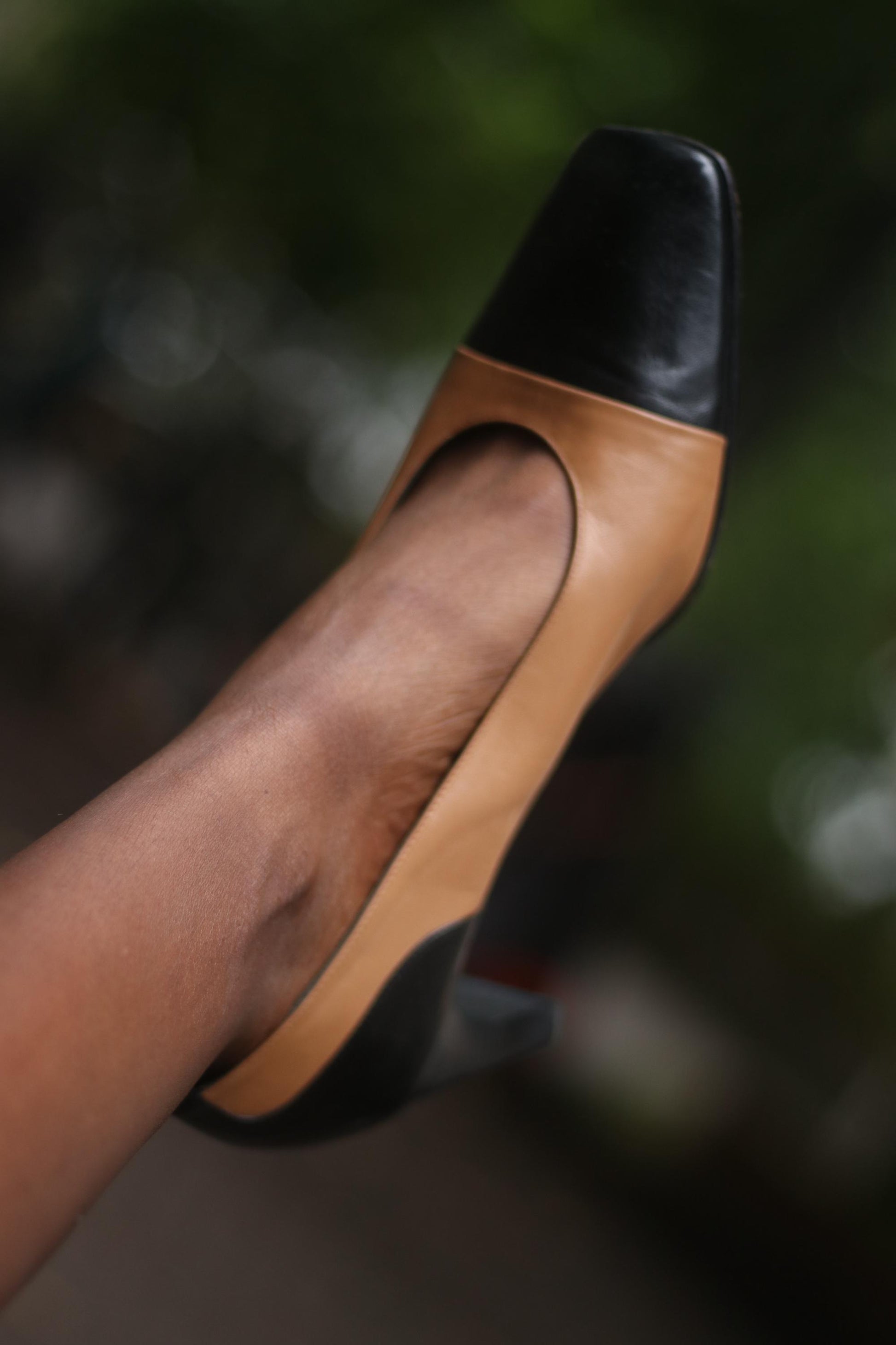 One vintage two-tone high heel in brown and black on a model&#39;s feet. The brand is Tanja Jannetti. The pump is photographed against a blurred background.