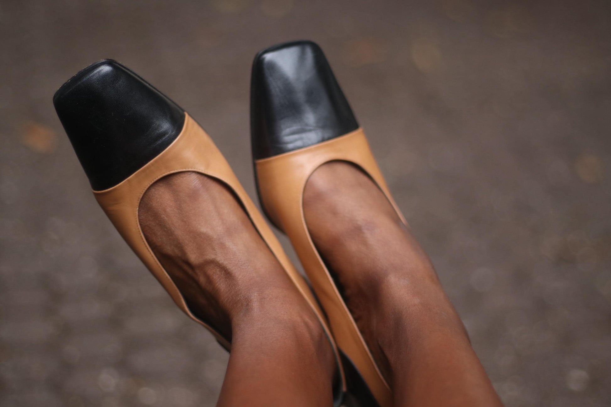 A pair of vintage two-tone high heels in brown and black on a model&#39;s feet. The brand is Tanja Jannetti. The chic pumps are photographed against a blurred background.