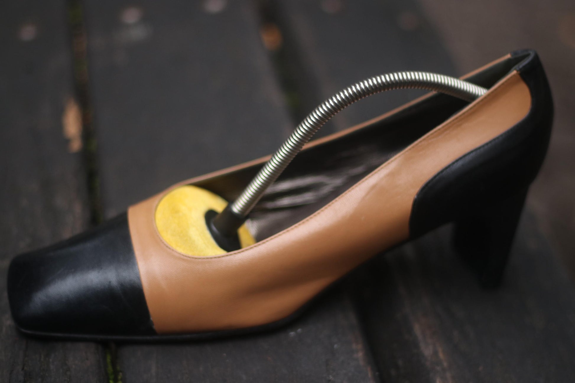 Vintage two-toned high heel shoe in brown and black with a metal spring inside, placed on a wooden surface.