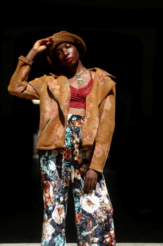 A woman of African heritage wearing a vintage Y2K floral jacket and maximalist floral pants. She also wears a hat, a red cropped lace top and two necklaces. The jacket is Italian-made and comes with two pockets for essentials.