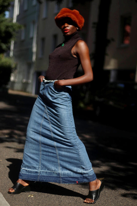 An outdoor shot of a female model wearing an Esprit Maxi Skirt from the early 2000s. The Vintage Low-Waisted Hippy Blue Jeans Skirt is styled with black sleeveless turtleneck and an oversized fuzzy brown newspaper boy hat  Bohemian Floral Embroidered Skirt