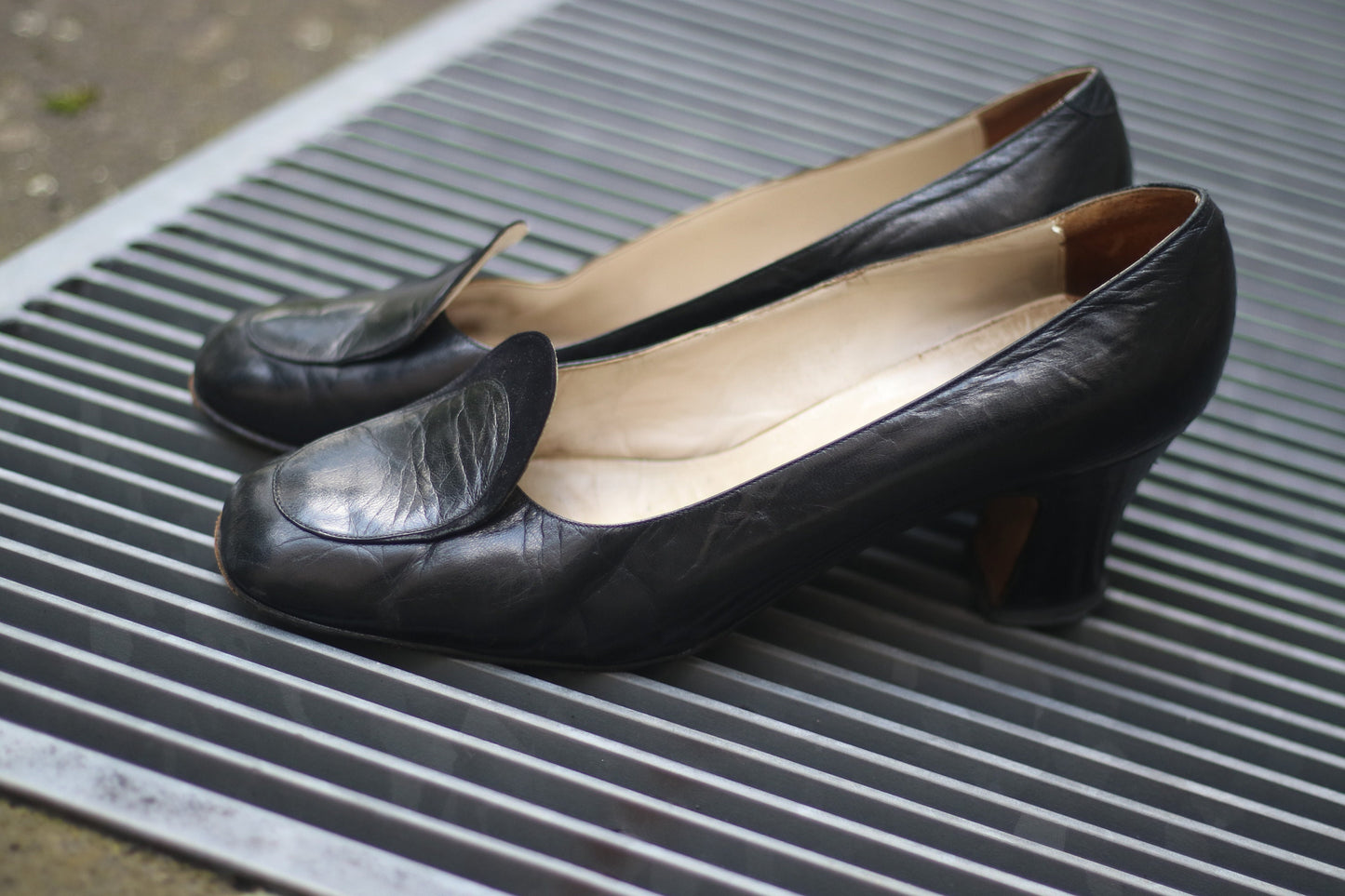 Vintage black leather high-heeled shoes with a rounded toe and mid heel, showcased on a concrete surface. Perfect for retro fashion enthusiasts and classic footwear collectors.