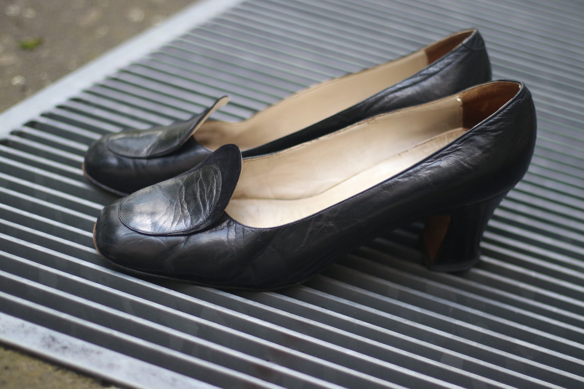 Vintage black leather high-heeled shoes with a rounded toe and mid heel, showcased on a concrete surface. Perfect for retro fashion enthusiasts and classic footwear collectors.