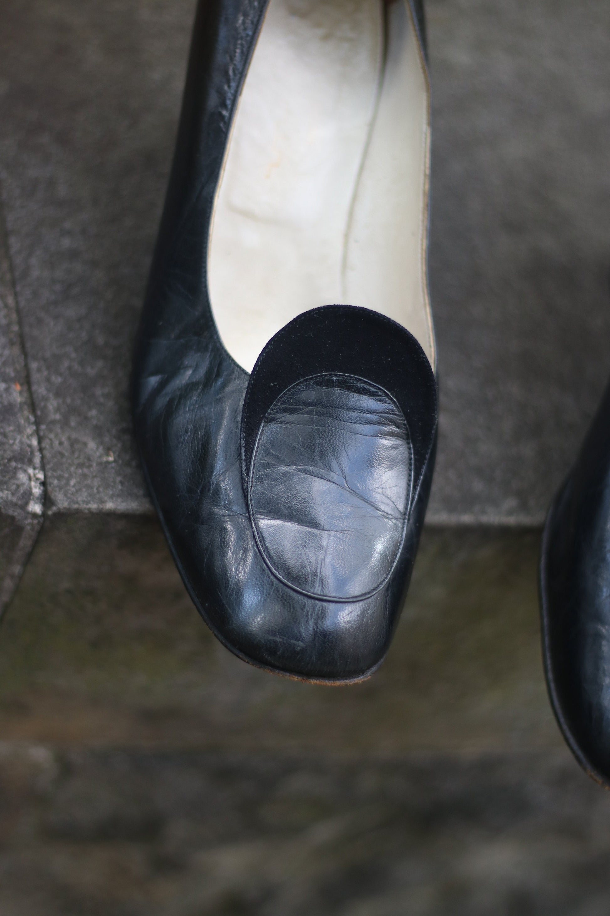 Vintage black leather high-heeled shoes with a rounded toe and mid heel, showcased on a concrete surface. Perfect for retro fashion enthusiasts and classic footwear collectors.