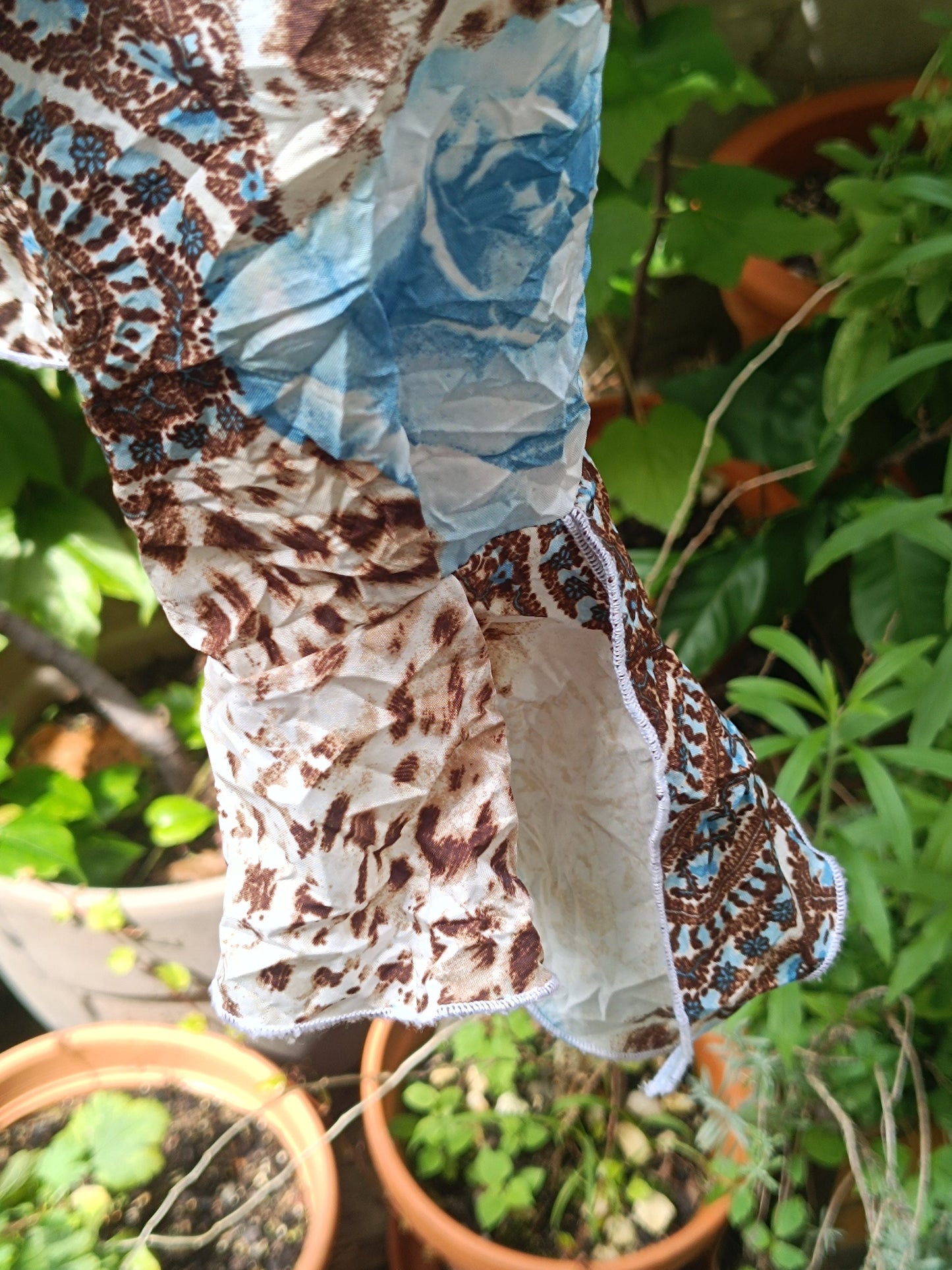 A closeup of the sleeves of  a vintage y2k floral print shirt with  by the brand BiBA photographed against a lush green background of plants