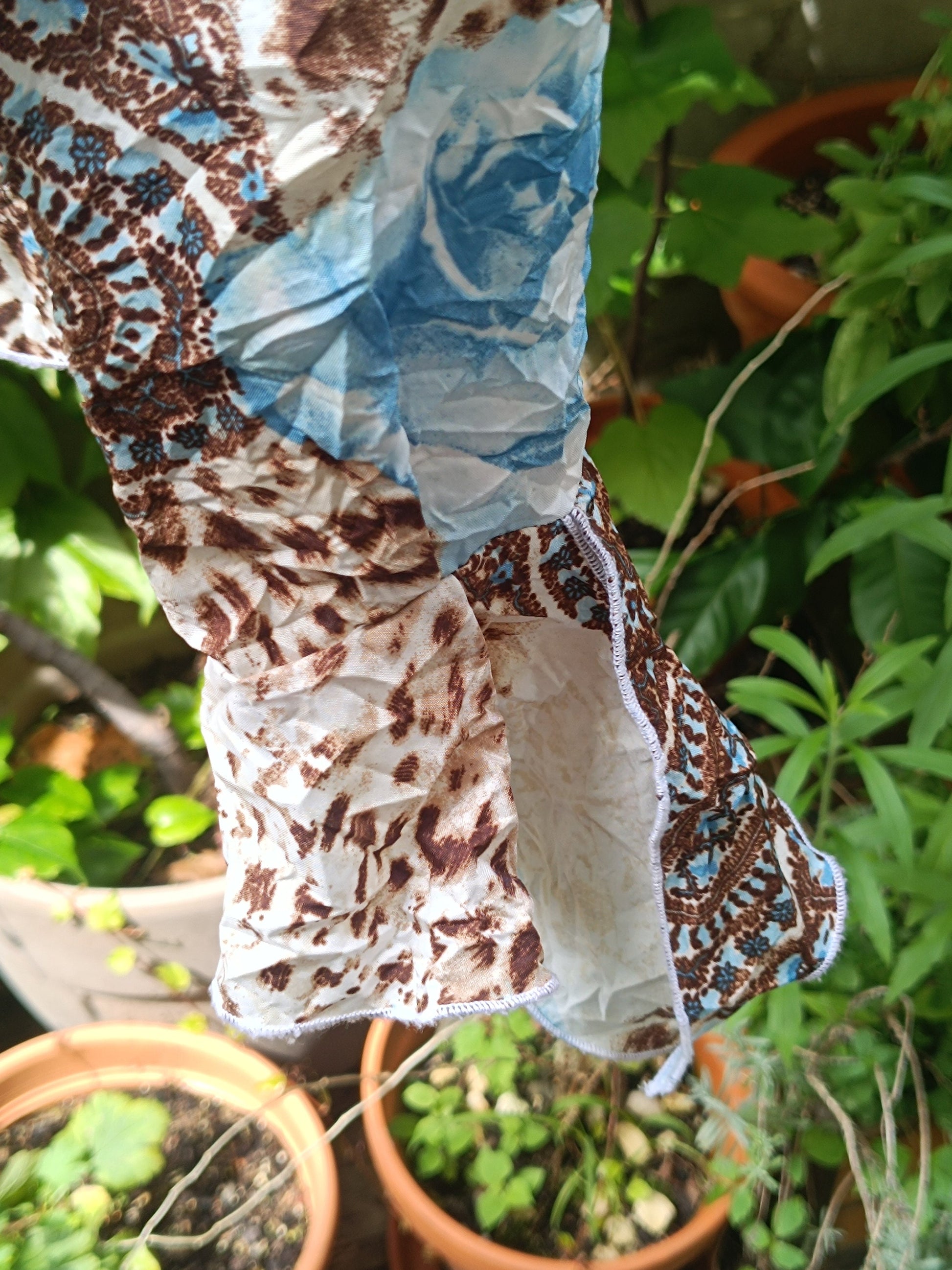 A closeup of the sleeves of  a vintage y2k floral print shirt with  by the brand BiBA photographed against a lush green background of plants