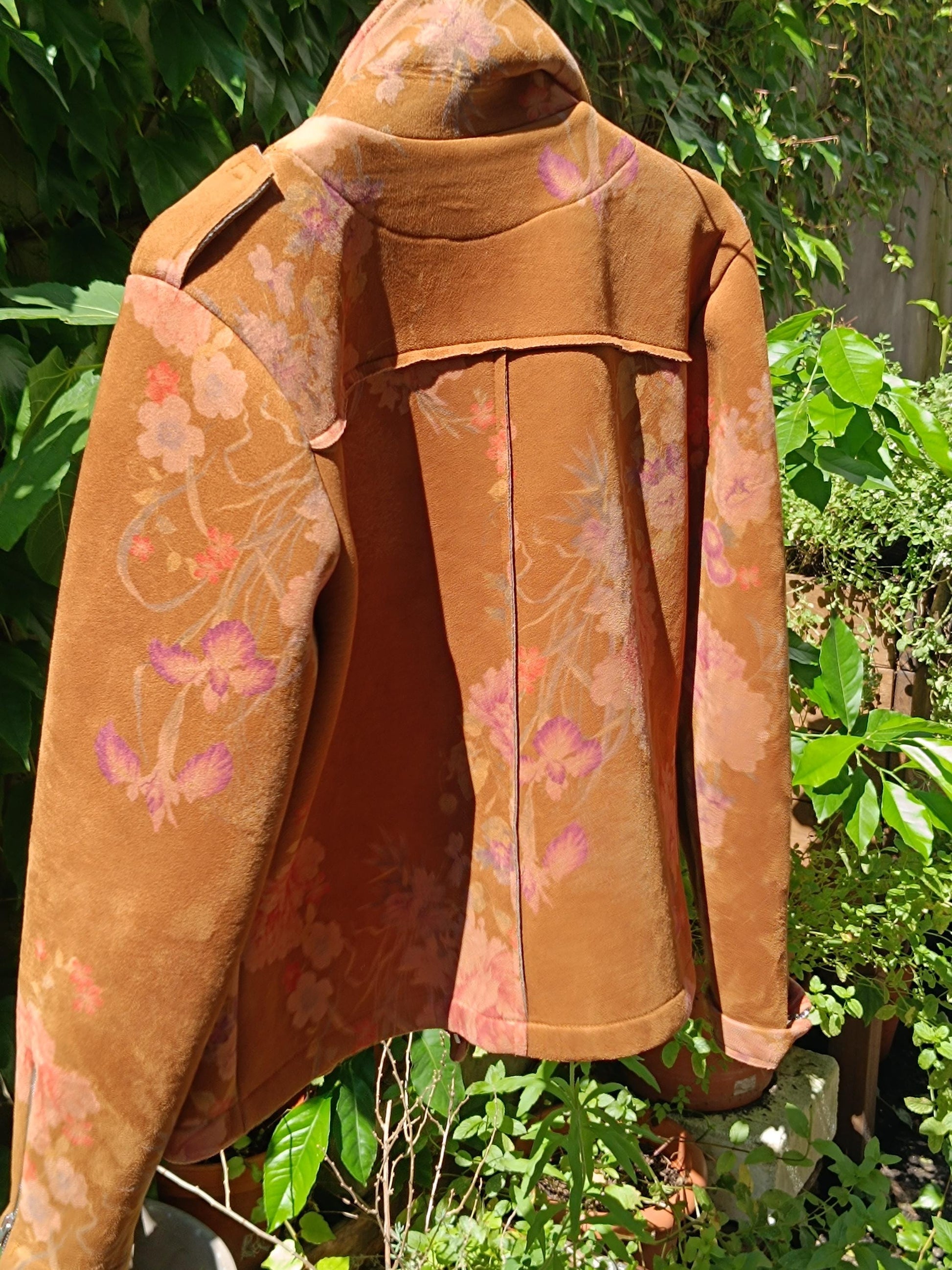 A still life photograph of the back of a vintage Y2K floral jacket. The jacket is on a hanger and is photographed against a background of green plants.