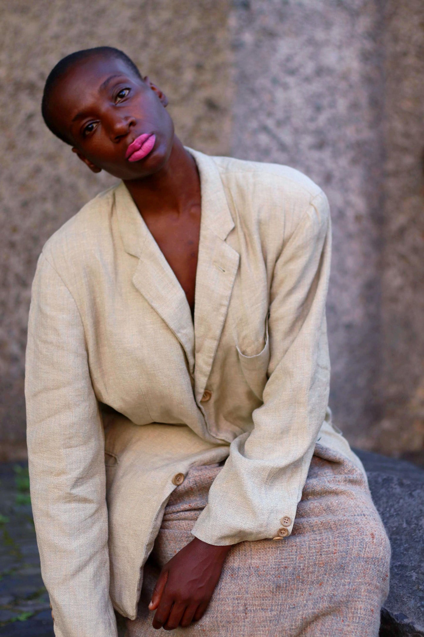 Model of African Heritage wearing a vintage Hugo Boss beige linen blazer  against a textured stone background, portraying a unique fashion style.