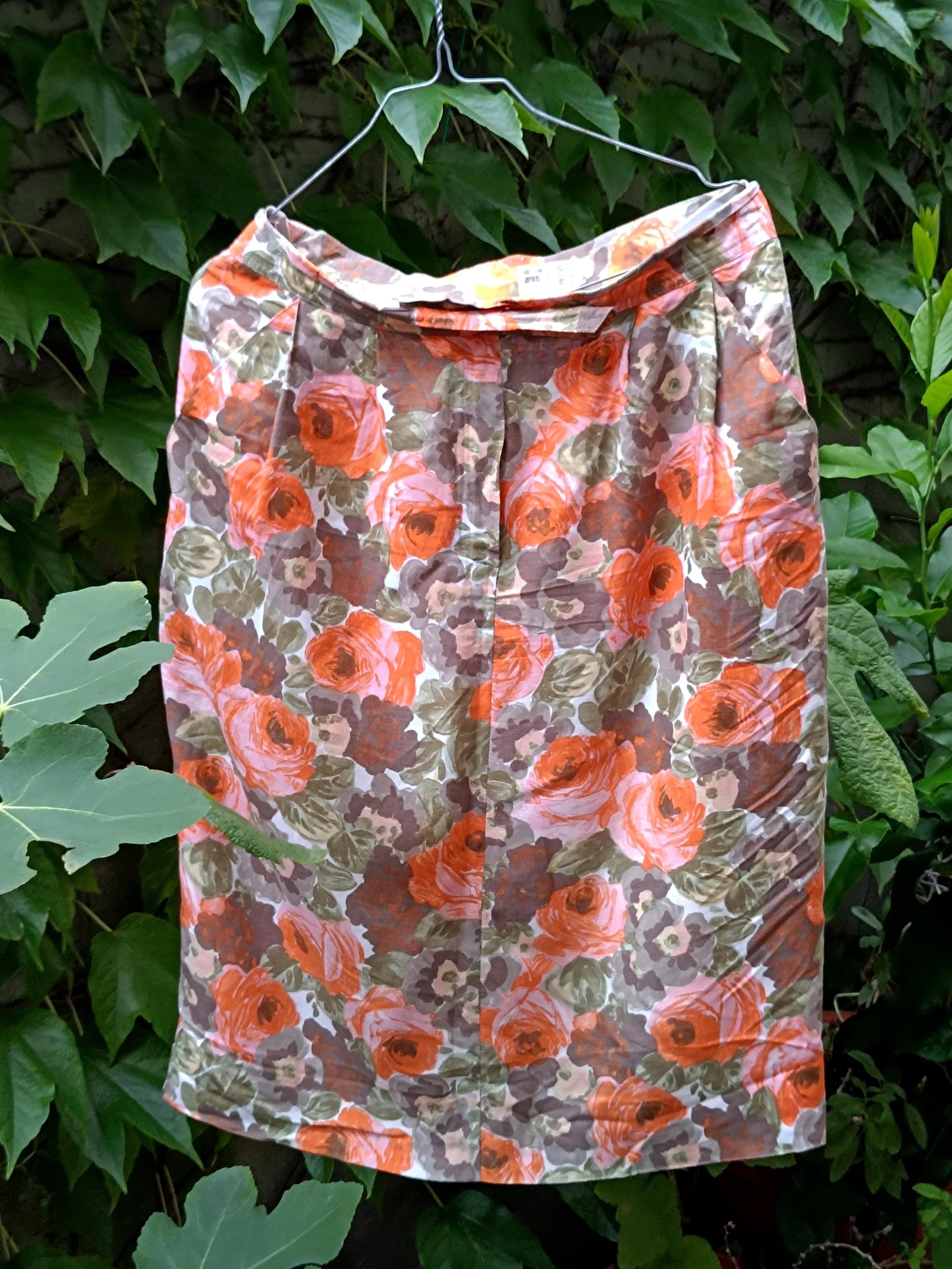 An artistic showcase of a vintage  floral from the 80s shot outdoors against a leafy background to highlight the bold orange blooms on a retro knee-length skirt