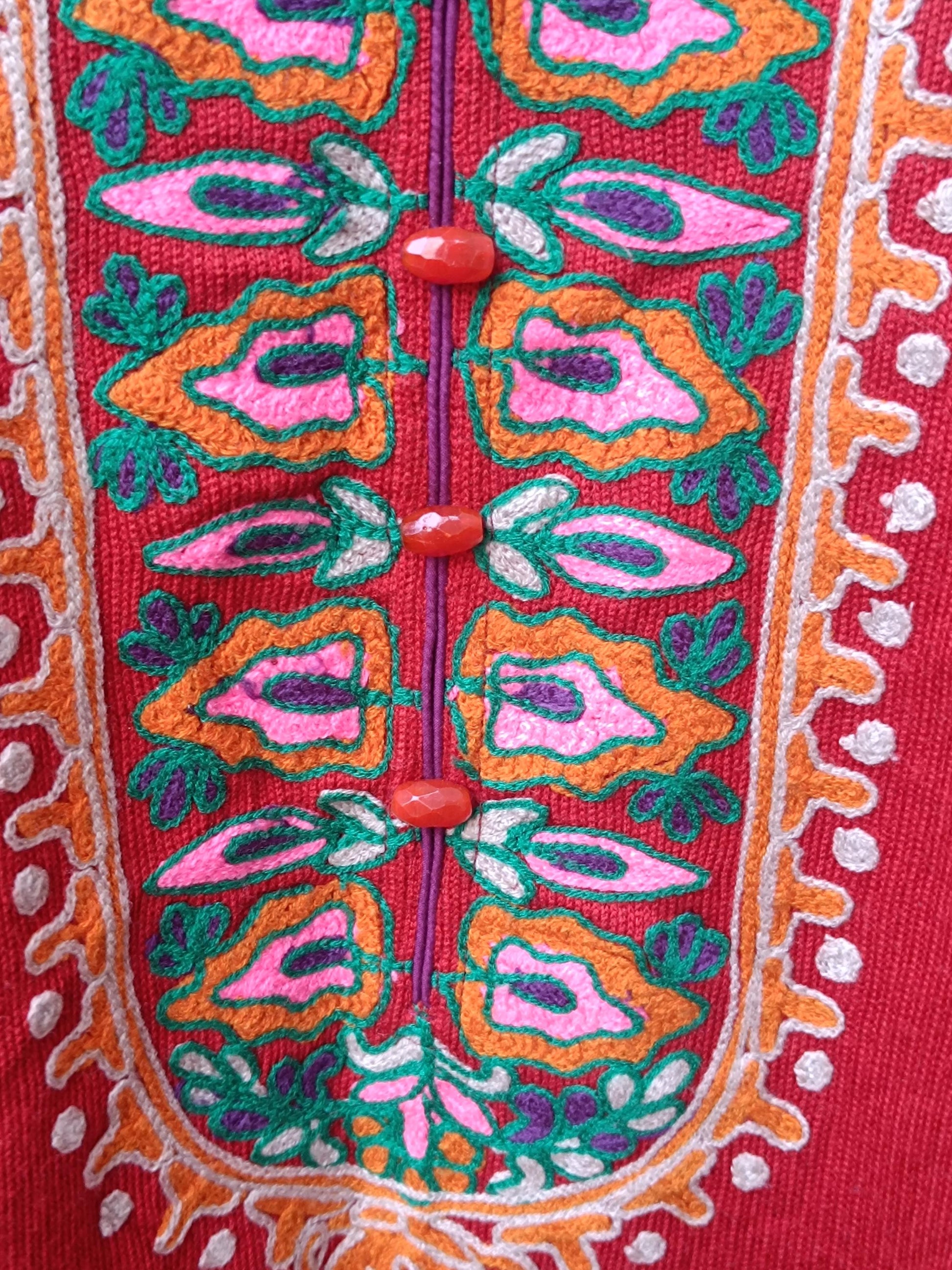 A close-up image of a folk-style red dress with colorful embroidered flowers and keyhole neckline. The photo zooms in on the bohemian feel by highlighting the whimsical buttons and floral details by the neckline