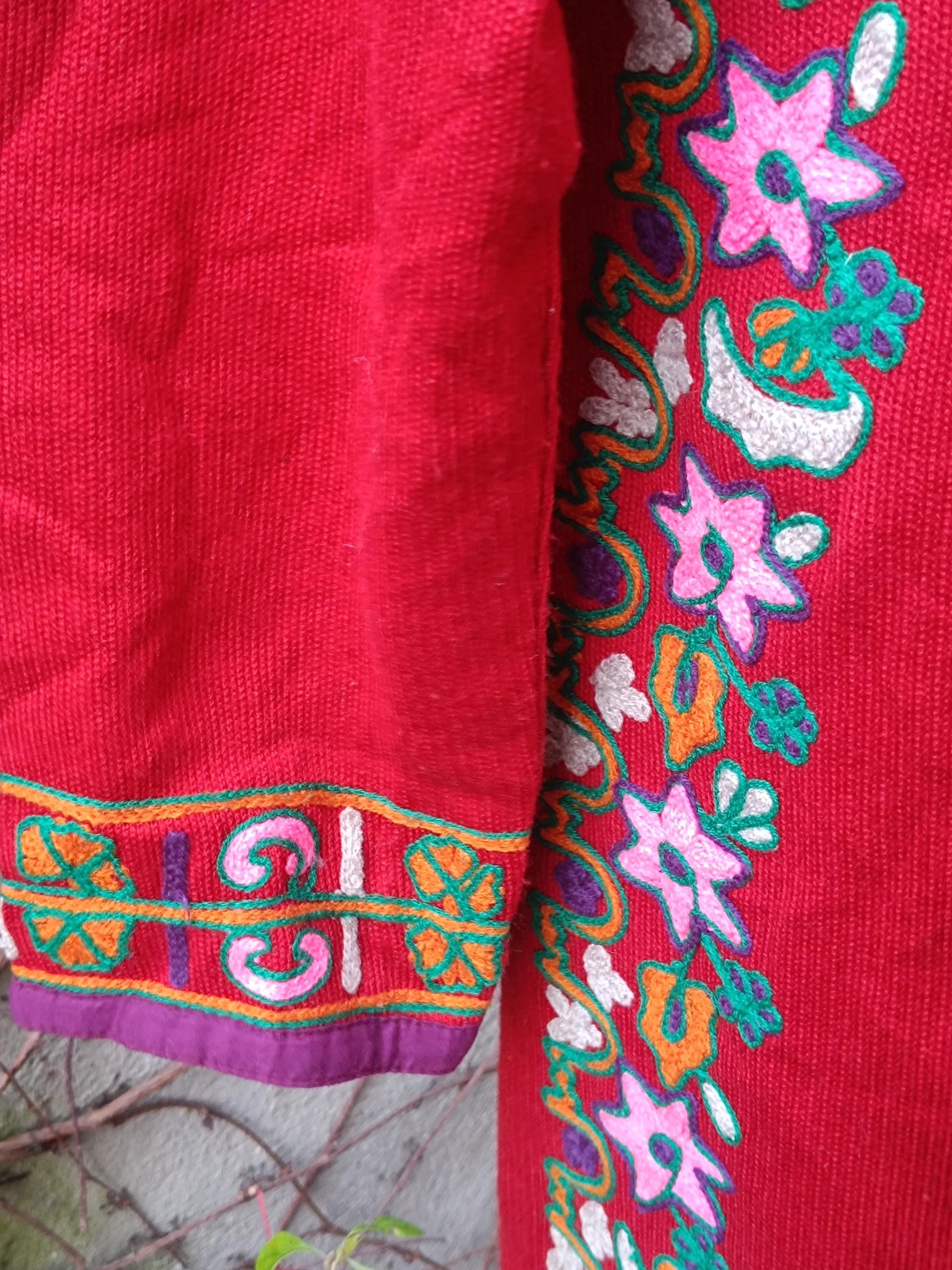A close-up image of a folk-style red dress with colorful embroidered flowers and keyhole neckline. The photo zooms in on the bohemian feel by highlighting the   floral details by the hemline
