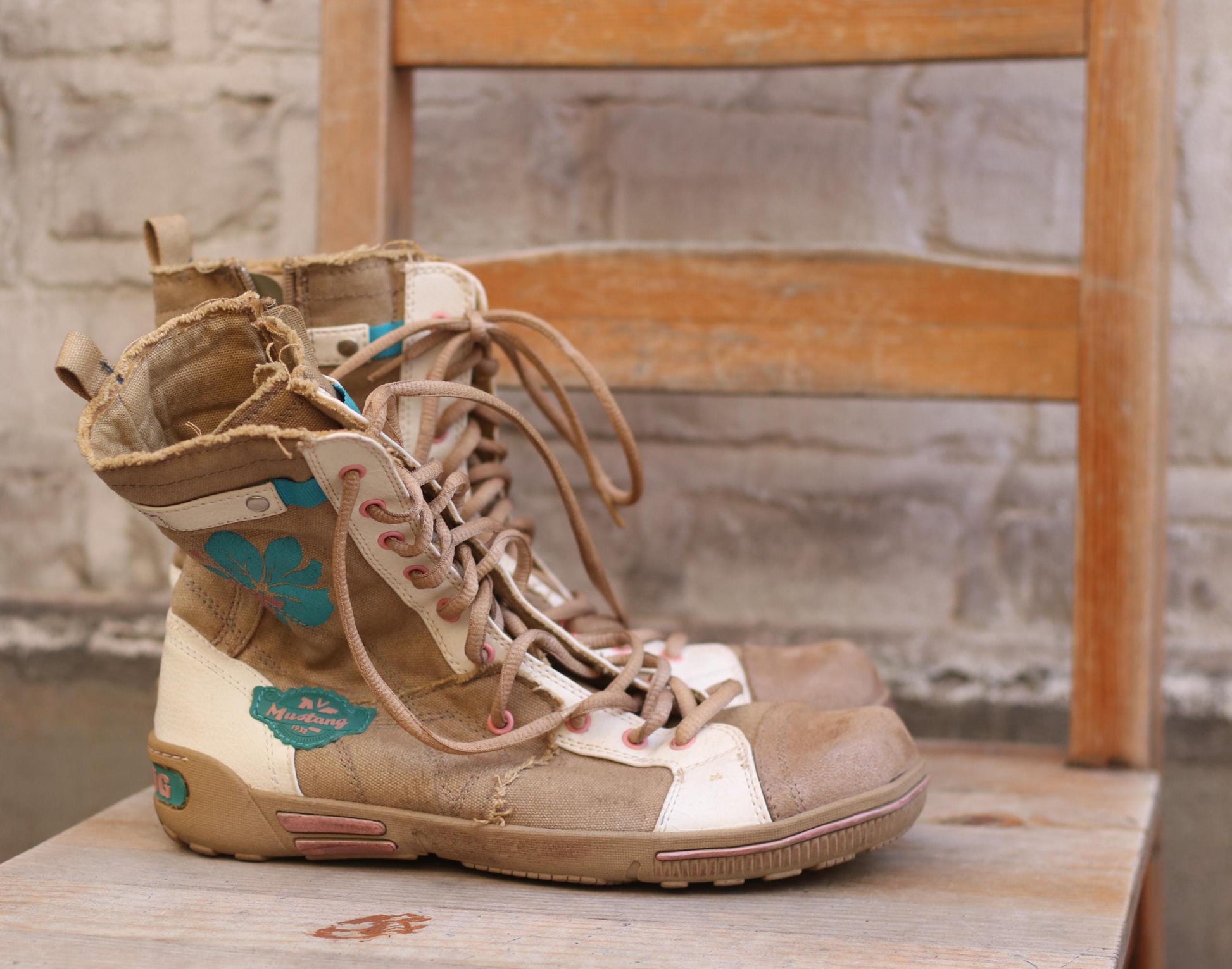 Vintage brown and beige canvas high-top sneakers by Mustang  with a blue leaf design, placed on a wooden chair in a rustic setting. Perfect footwear for a casual, retro-inspired style.