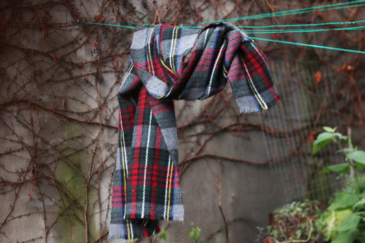 Vintage Tartan plaid scarf hanging on a line against a textured wall with climbing vines, outdoor setting, The 90s design in red , grey and green tones is a sustainable winter fashion accessory.