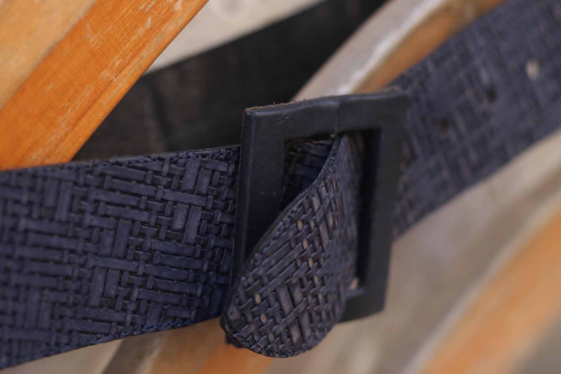 Blue woven belt draped over the back of a wooden chair against a textured brick wall background.