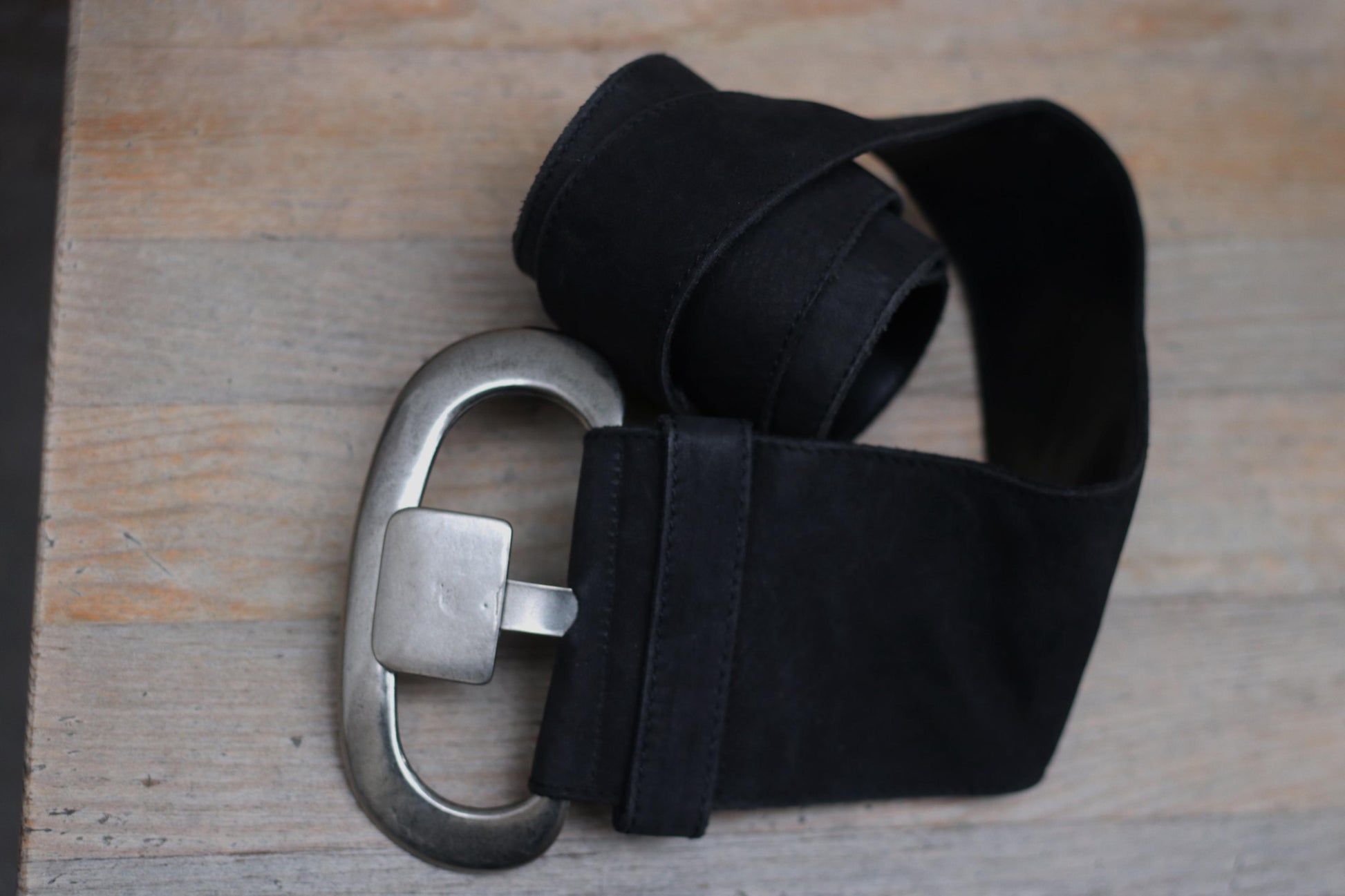Close-up of a stylish black leather belt by Marc Cain. The vintage belt touts  a silver buckle and is photographed on a wooden table. Perfect fashion accessory for enhancing outfits with a touch of elegance and sophistication.
